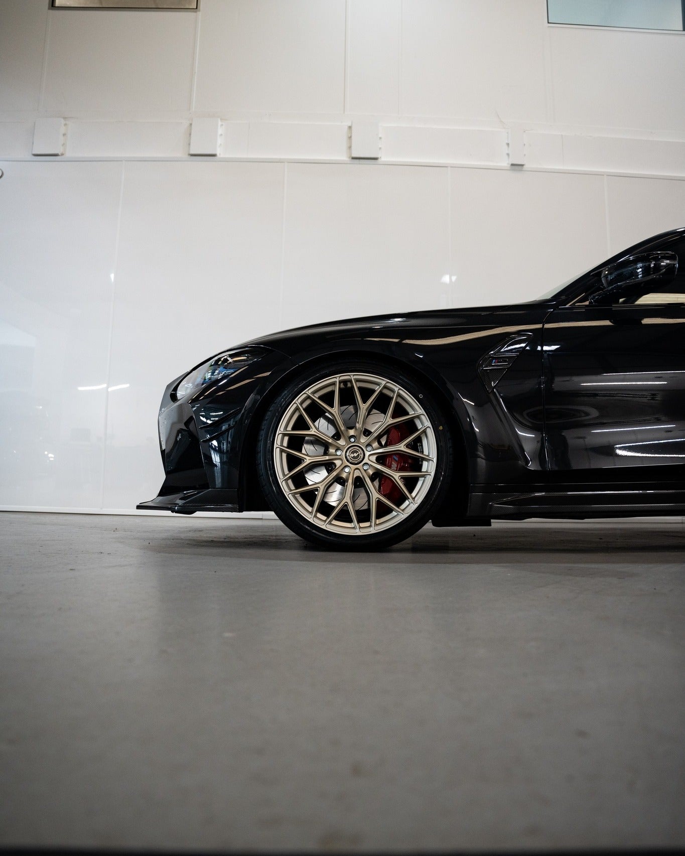 Front of an M3 G80 with Frozen Gold M-WX's and on Motech Stance springs in a car workshop.