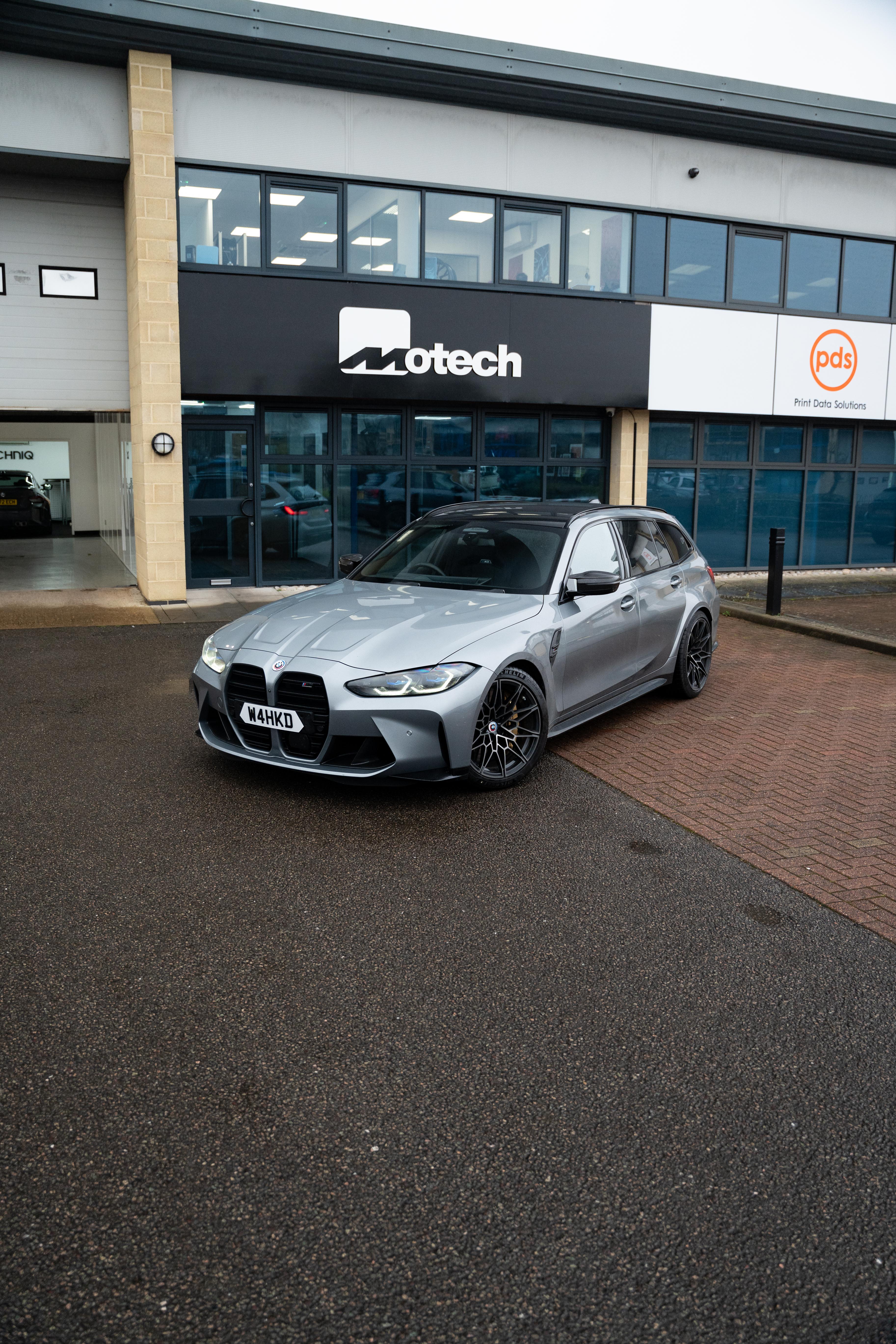 Grey BMW M3 on Motech Stance springs outside a building with 'Motech' branding.