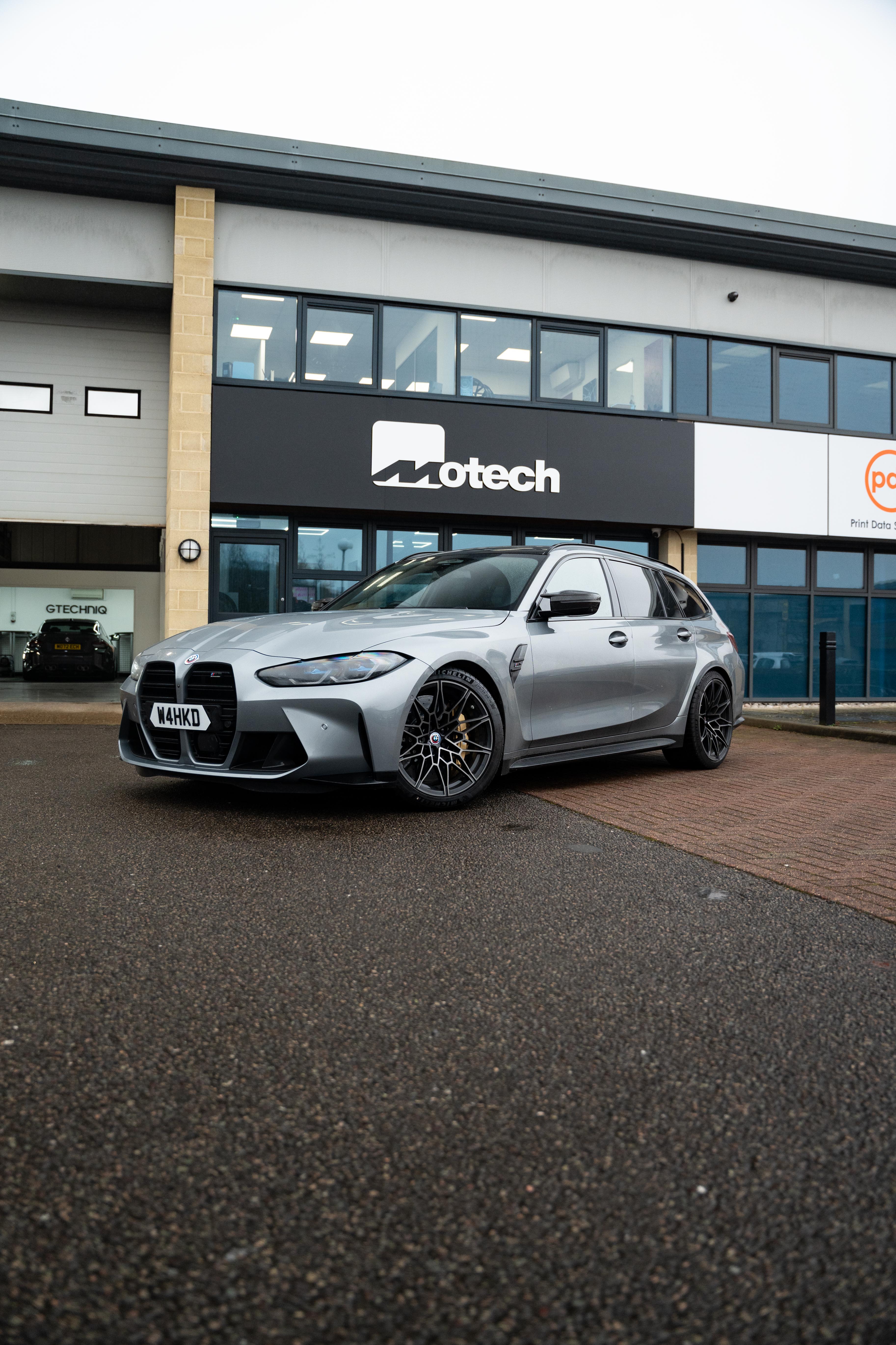 Grey BMW M3 on Motech Stance springs outside a building with 'Motech' branding.