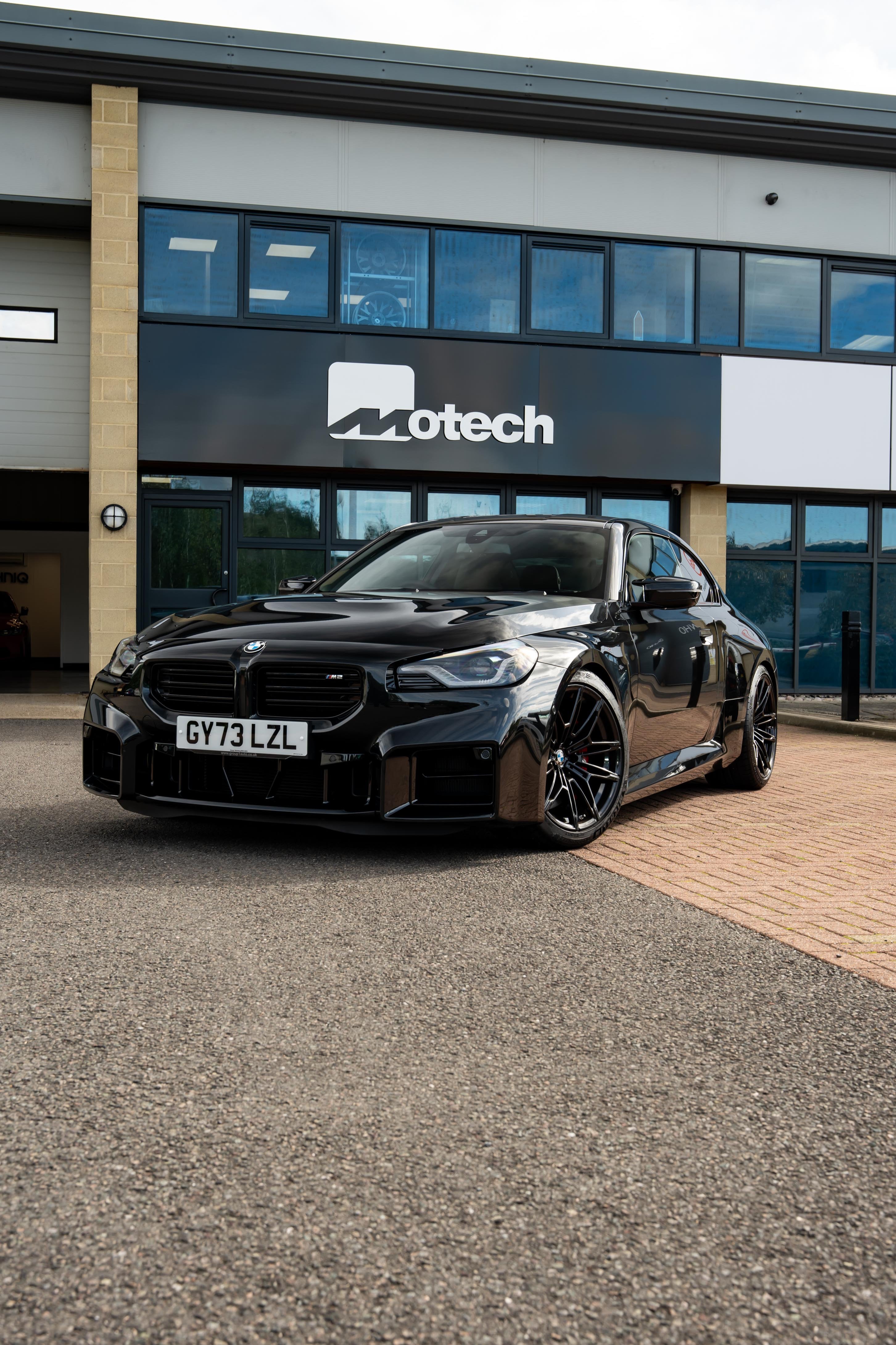 Black BMW M2 G87 on Motech Stance Springs parked outside a building with 'Motech' branding.