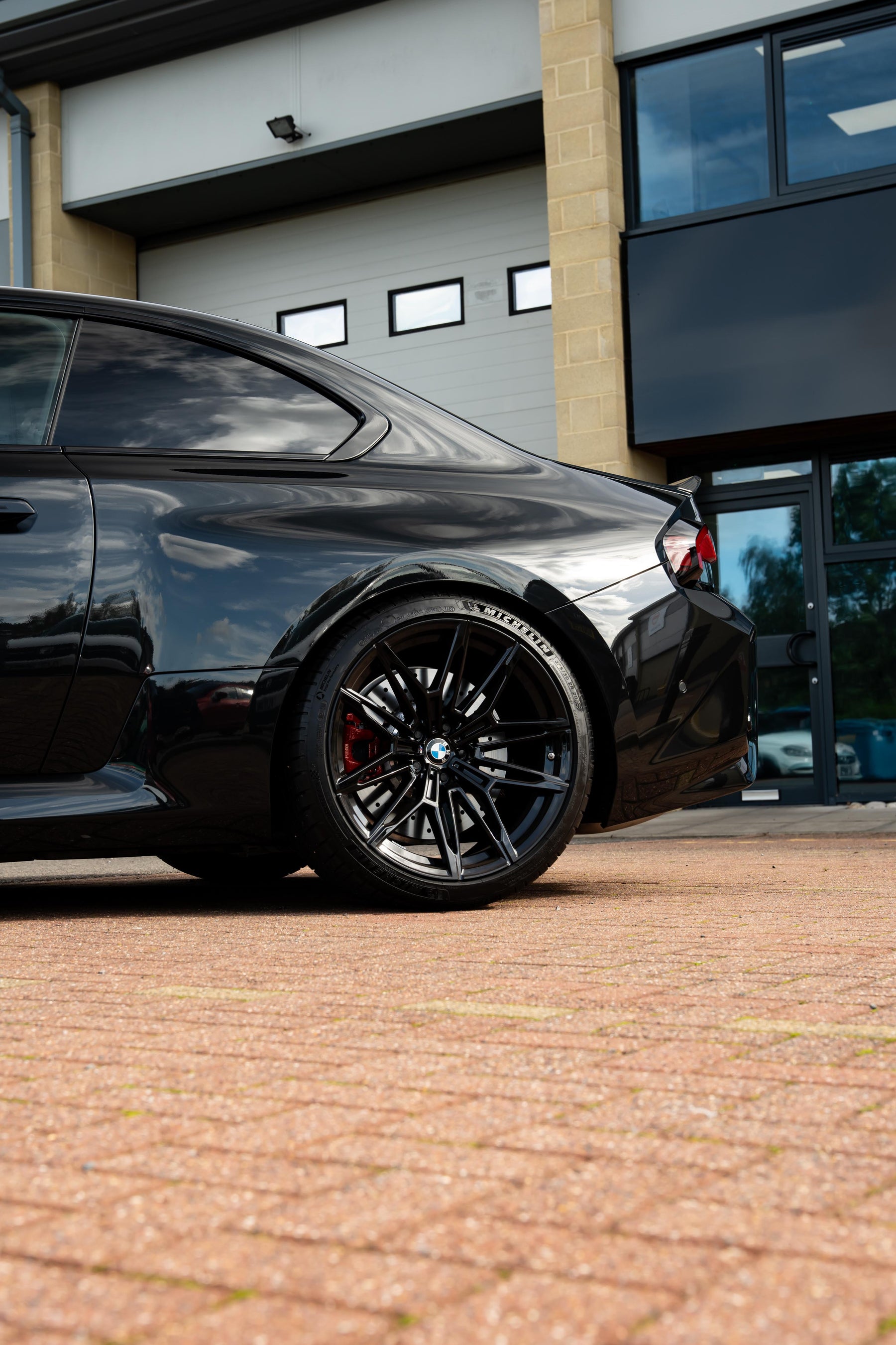 Black car parked in front of a building with red bricks on the drive.