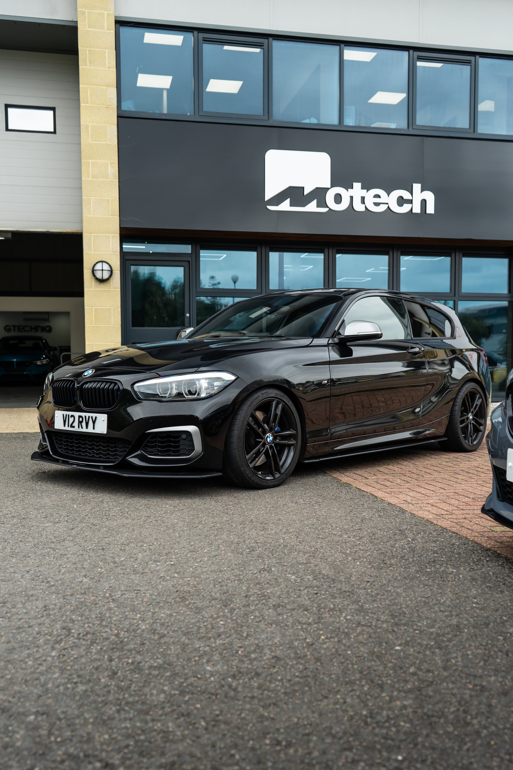 A black BMW 1 Series outside Motech with Motech Stance springs.