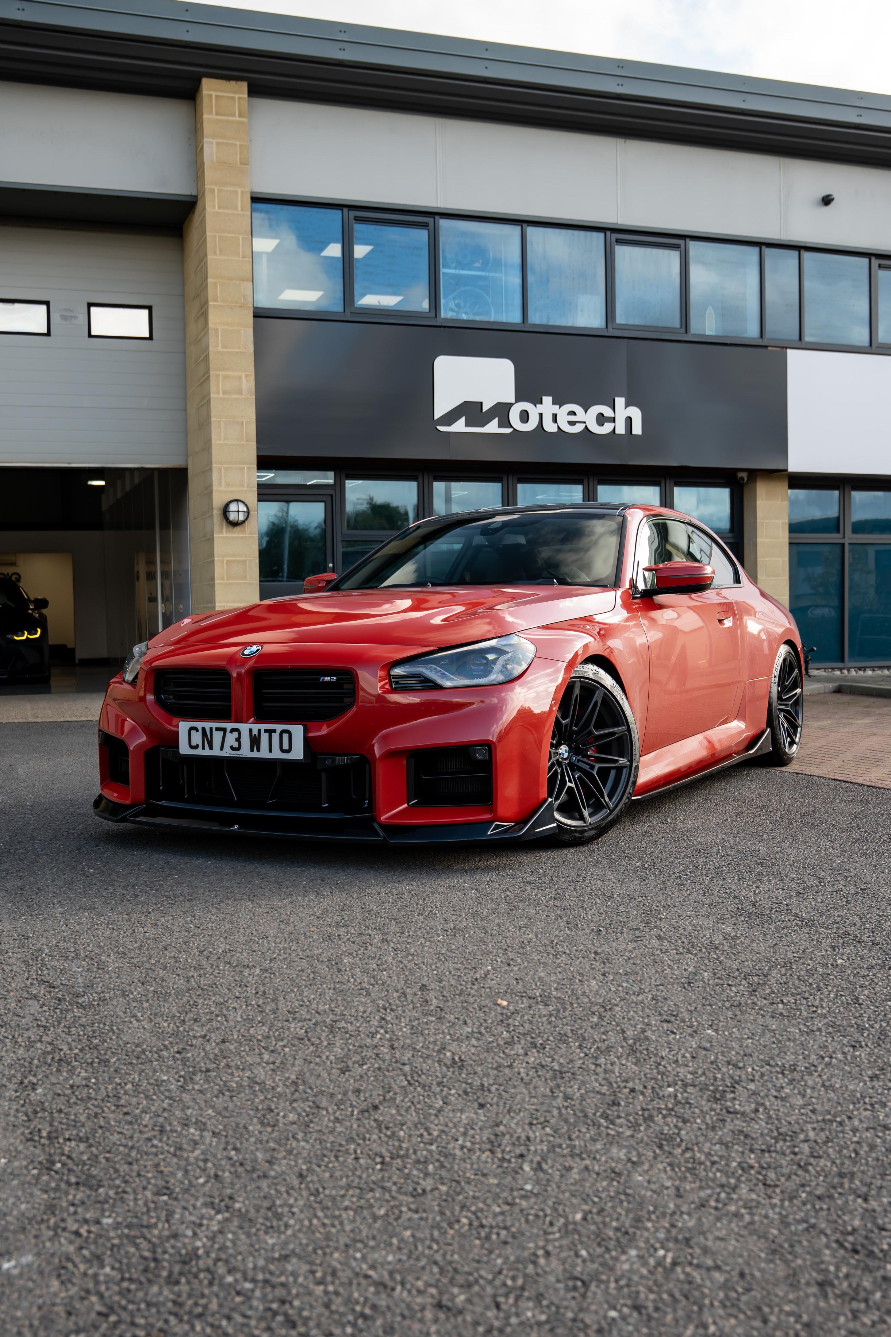 Red BMW M2 G87 on Motech Stance Springs parked outside a building with 'Motech' branding.