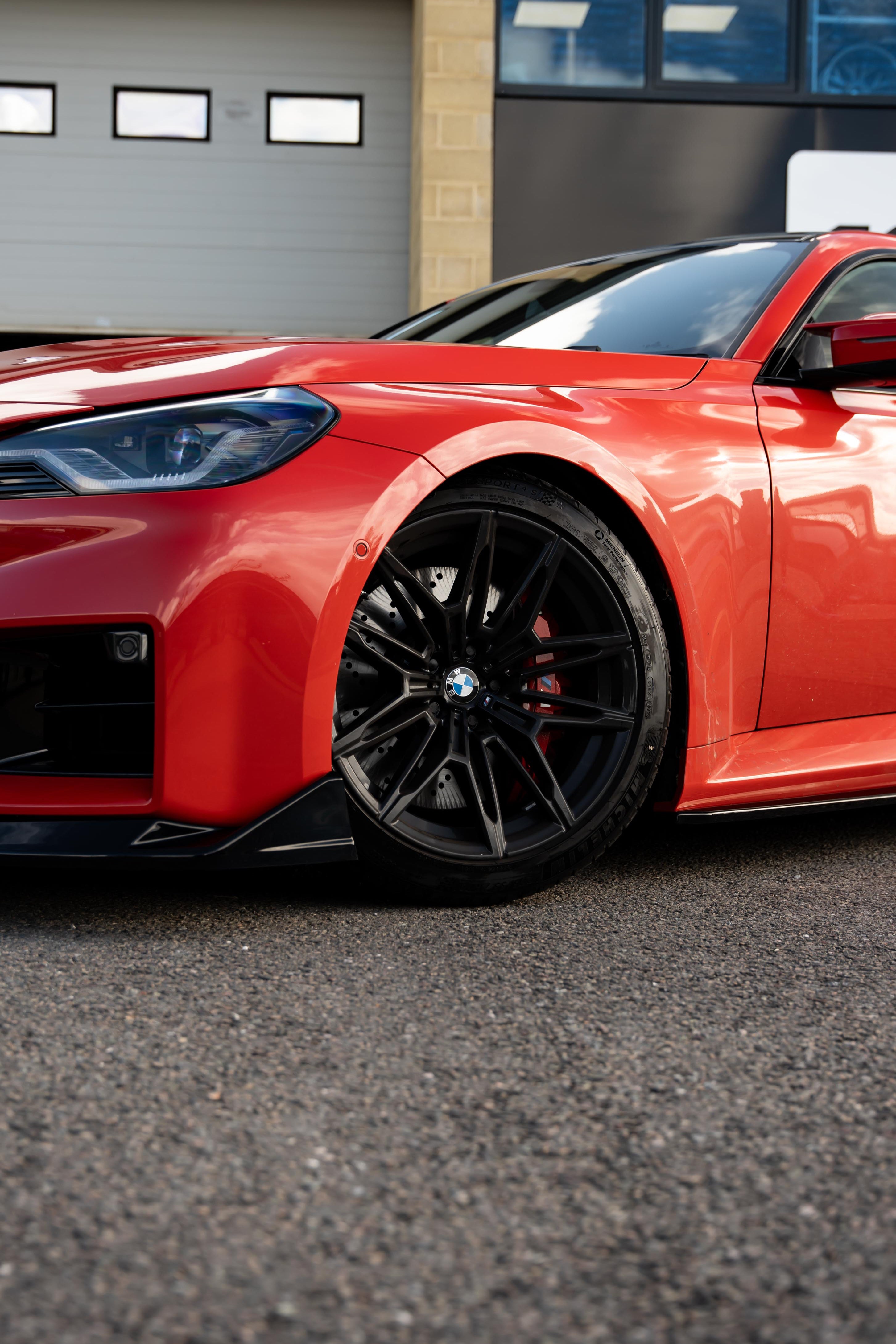 Red sports car with black rims parked in front of a building