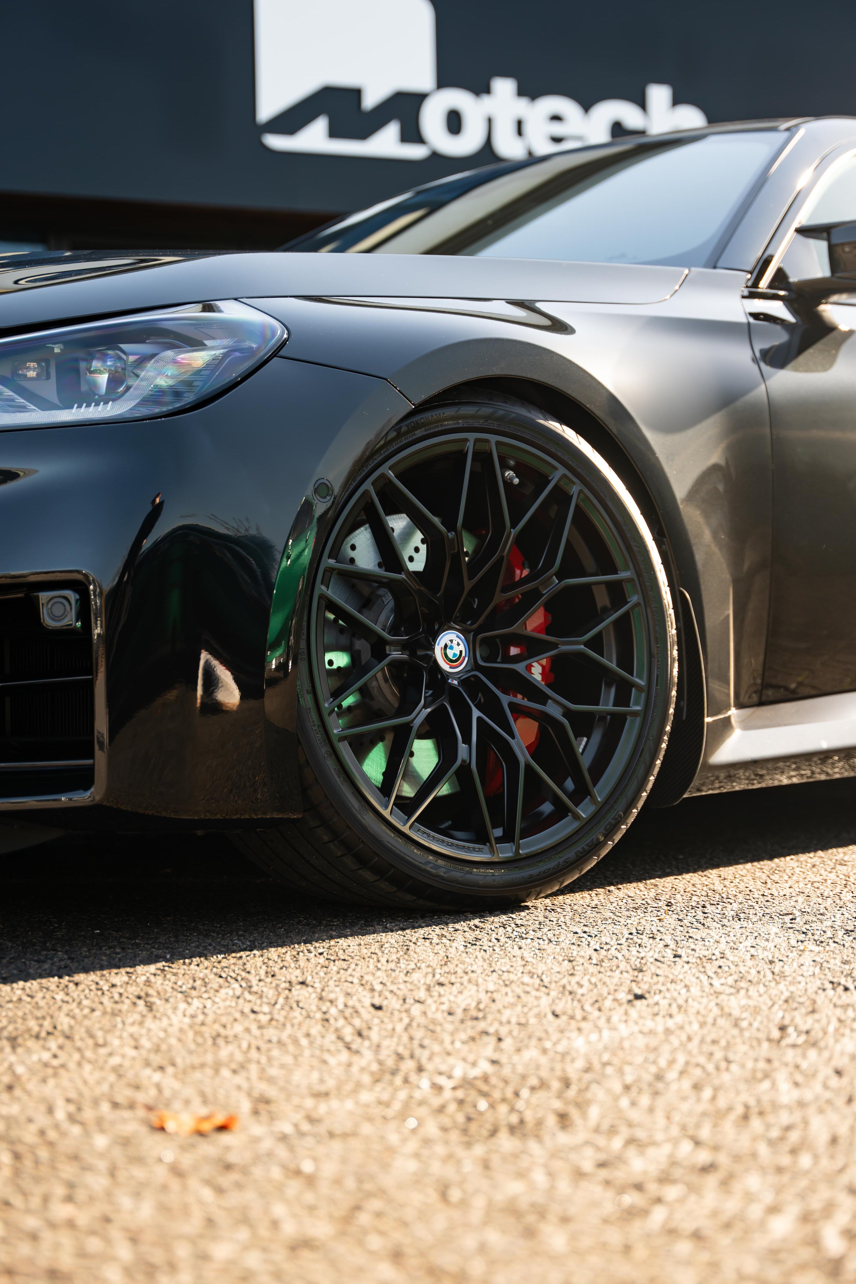 Close-up of a black car's wheel with Motech branding in the background.