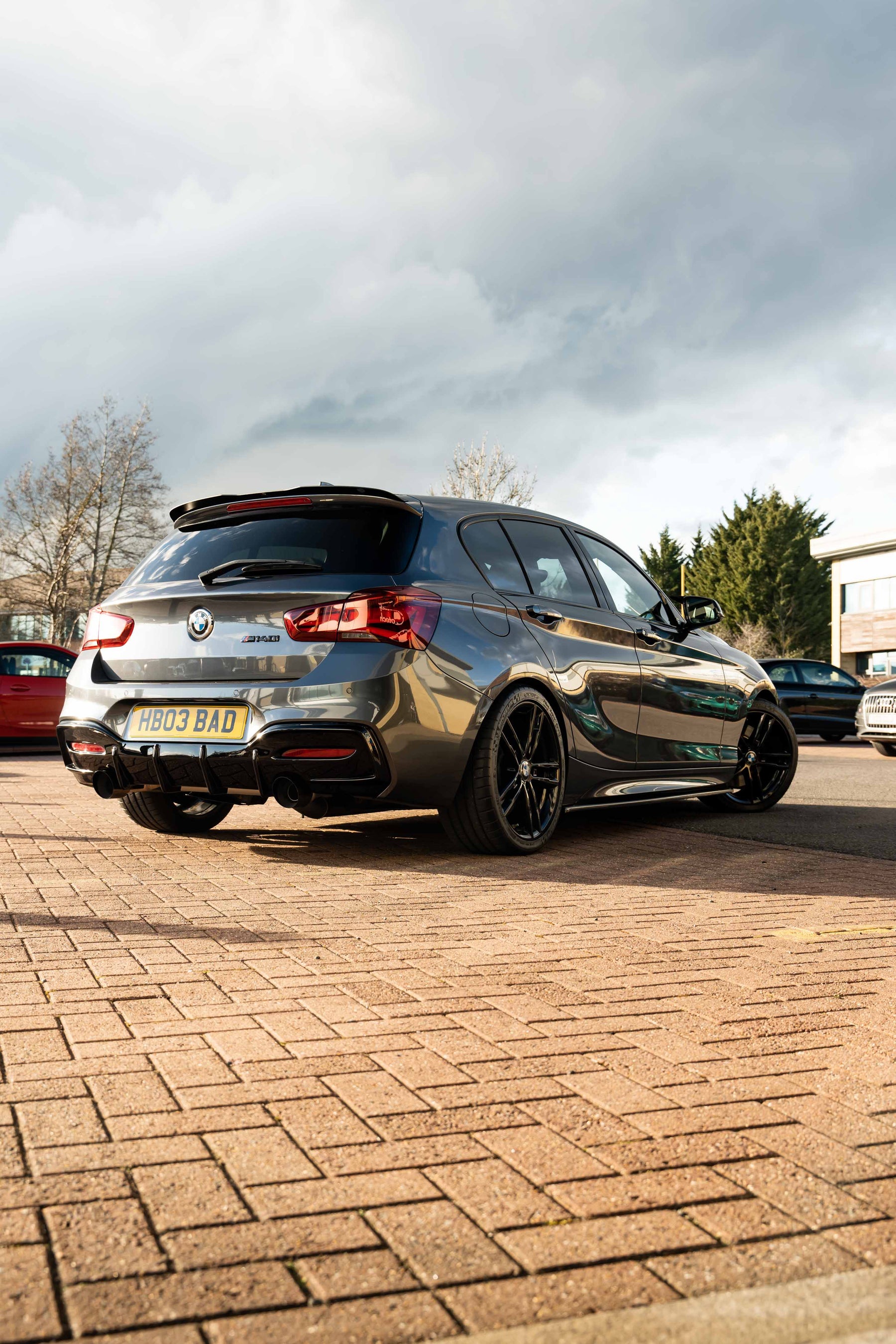 Grey BMW car with Motech Stance Springs on a brick driveway with a cloudy sky.