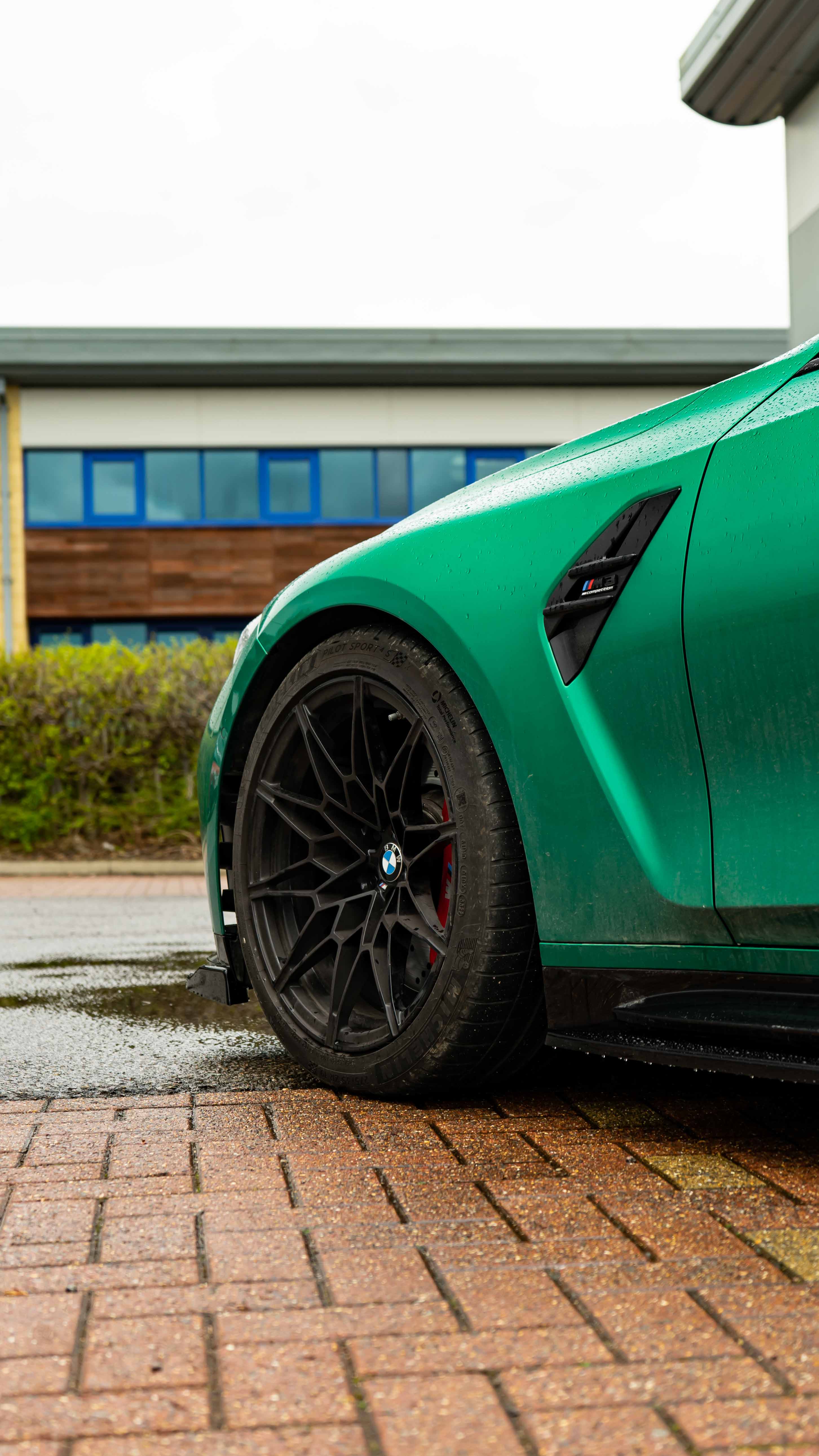 Front of a Green BMW M3 G80 on Motech Stance springs parked outside a building with 'Motech' branding.