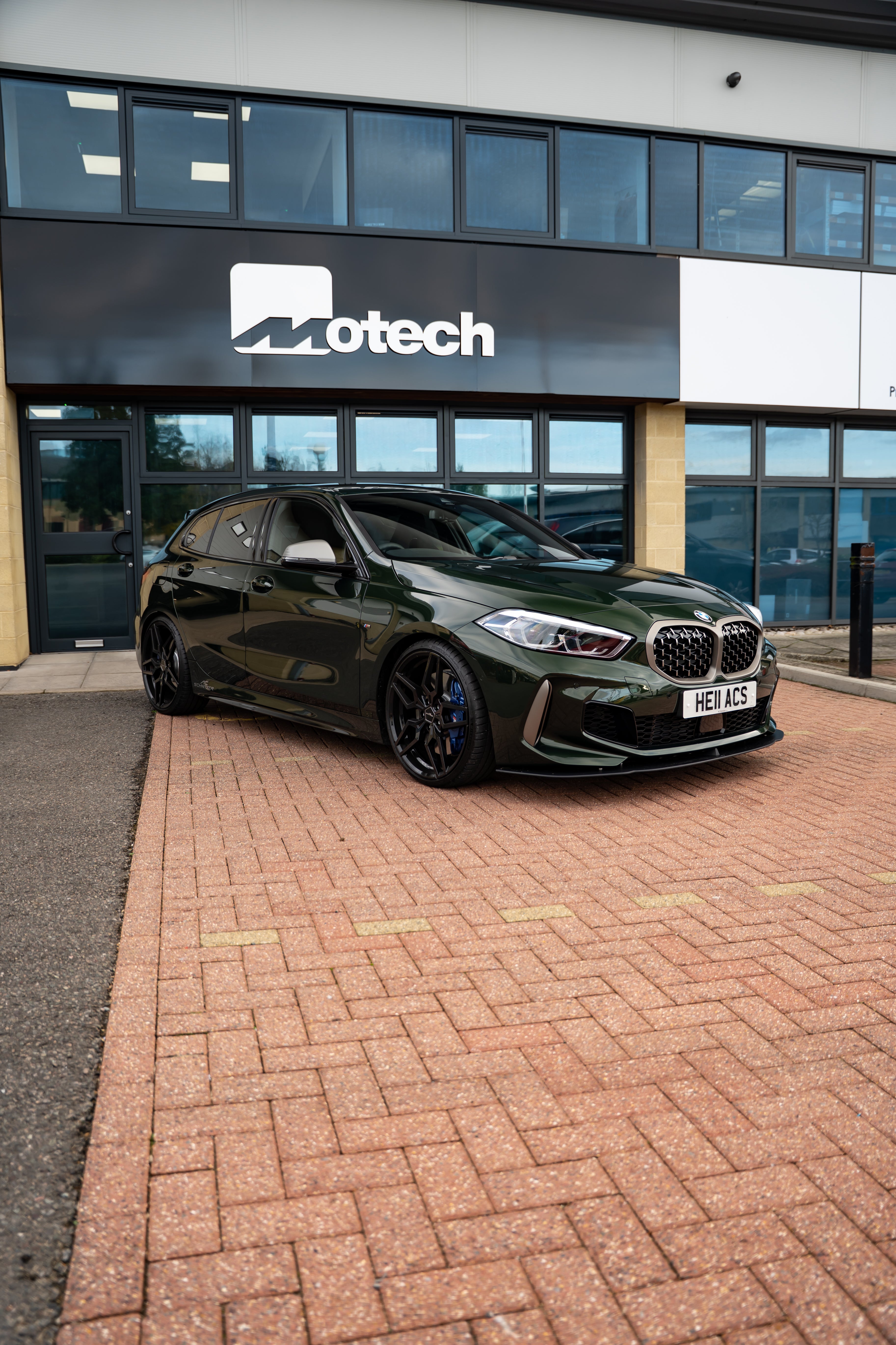 Green car with an AC Schnitzer Front Splitter parked in front of a building with 'Motech' branding.