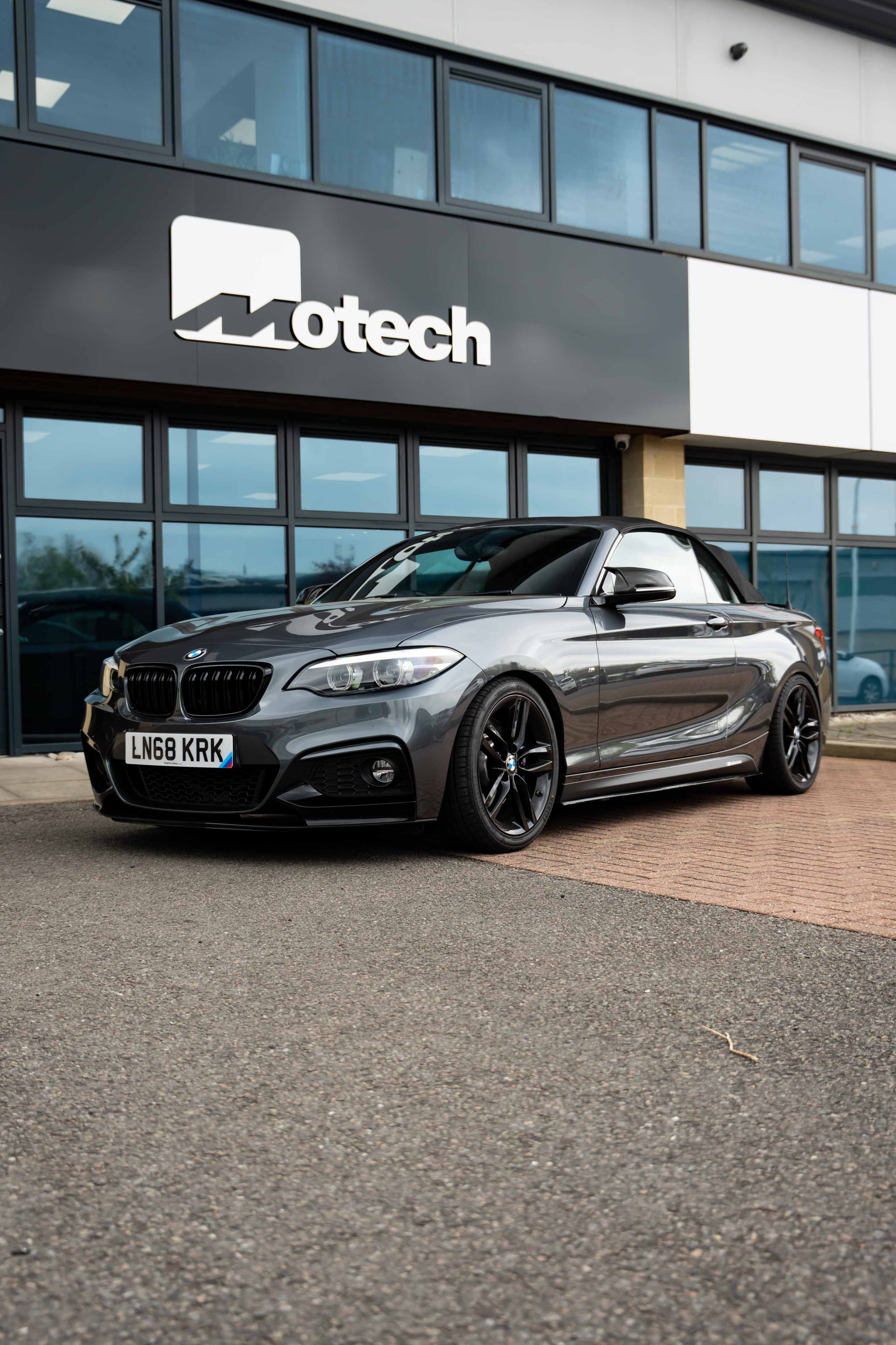 Silver BMW on Motech Stance Springs parked in front of a building with 'Motech' branding.