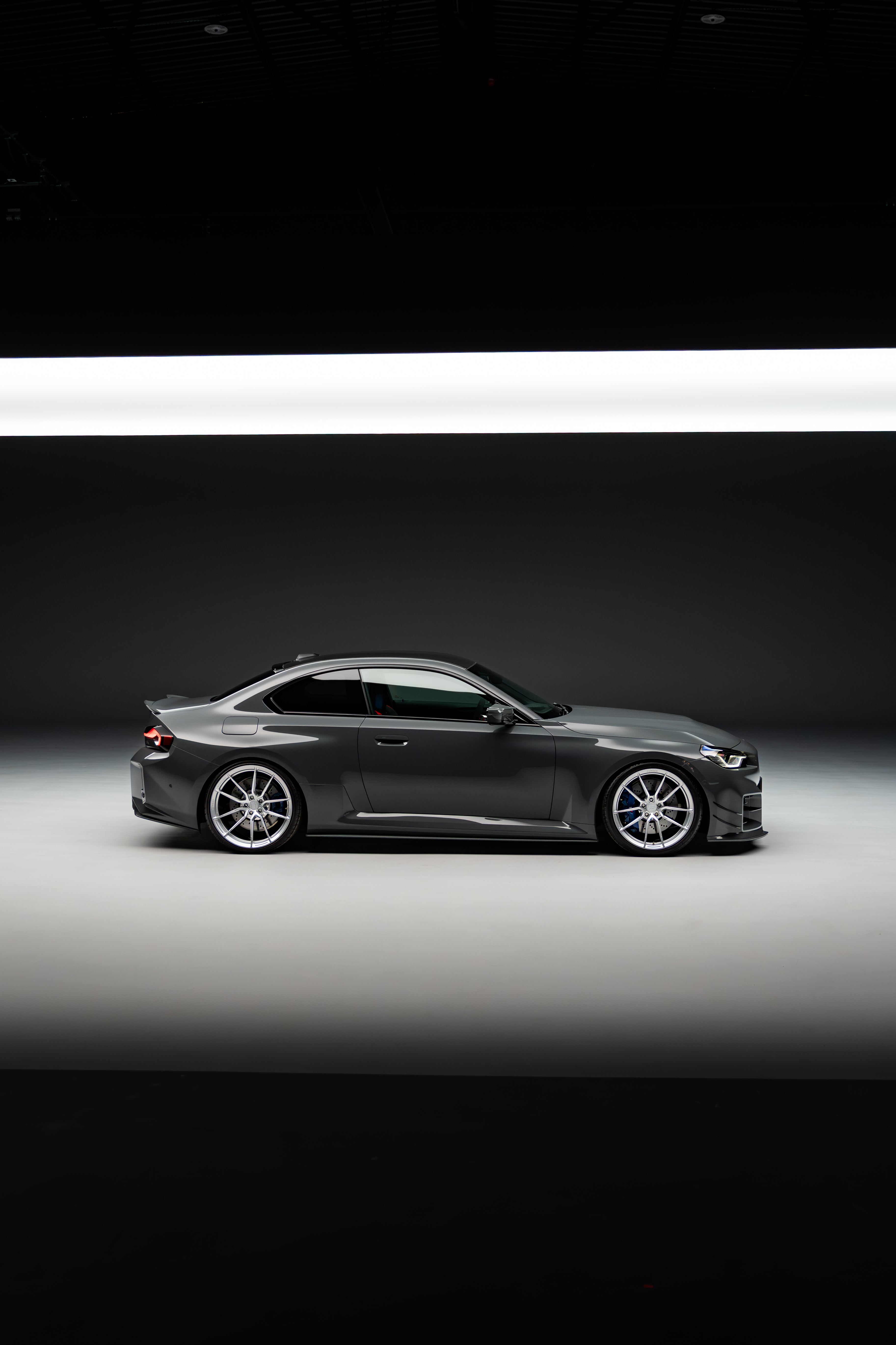 Side-on shot of a BMW M2 G87 with aftermarket wheels and lowered on springs in a high-quality photography studio.