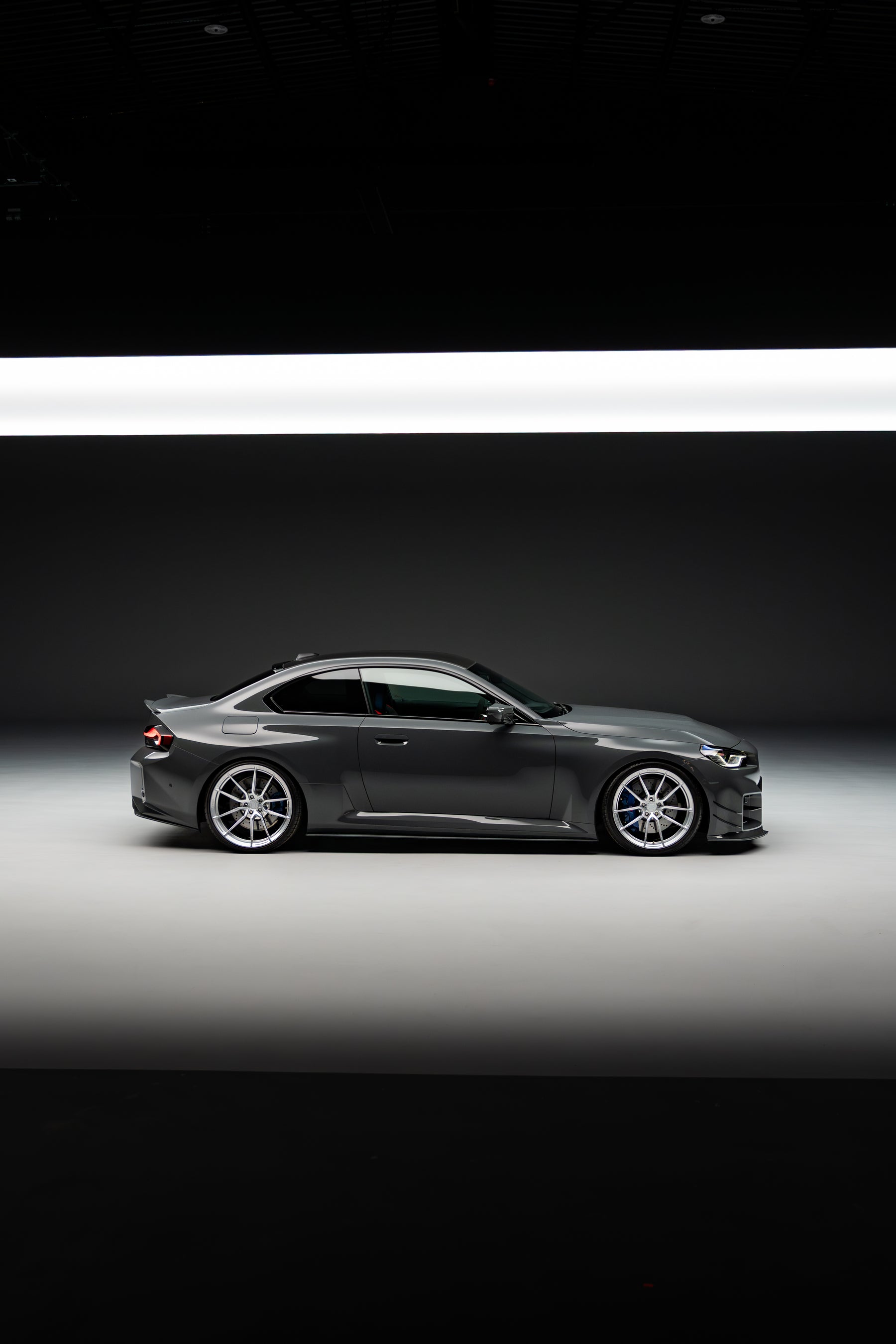 Side-on shot of a BMW M2 G87 with aftermarket wheels and lowered on springs in a high-quality photography studio.