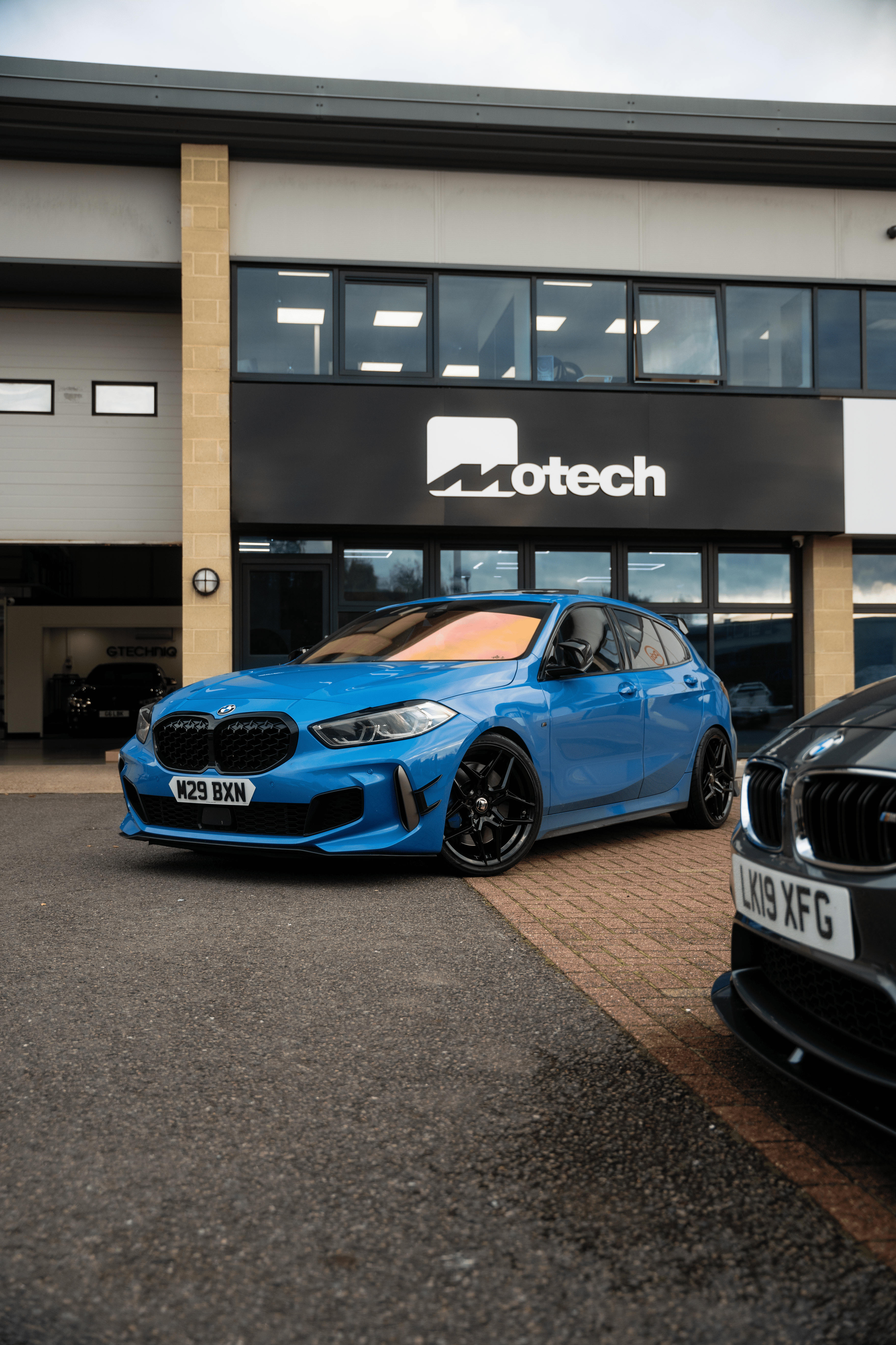 Blue car on Motech Stance Springs parked in front of a building with 'Motech' branding