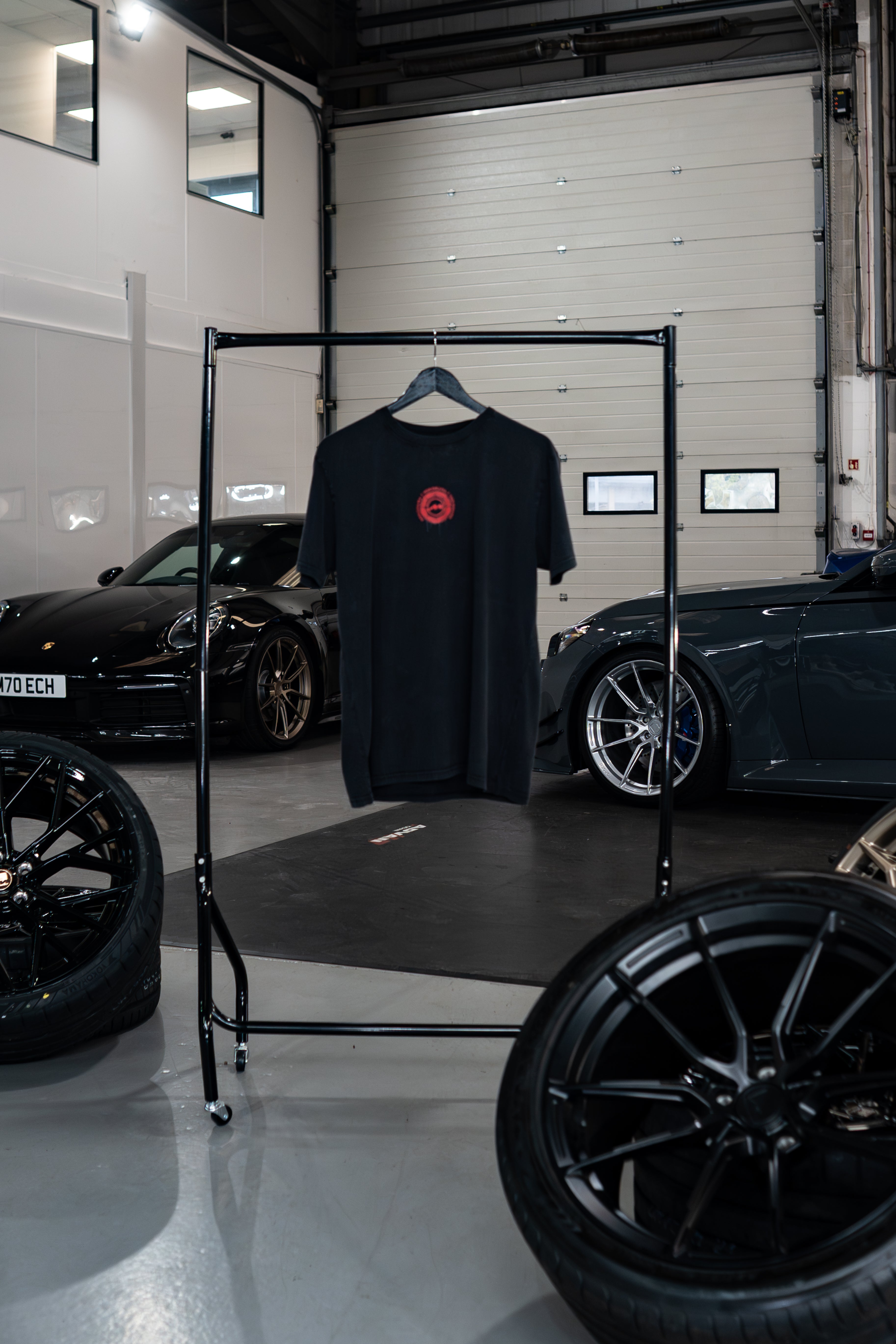 Treadlight Collection Stone Washed T-Shirt with a red logo on a rack in a garage setting with cars and tires.