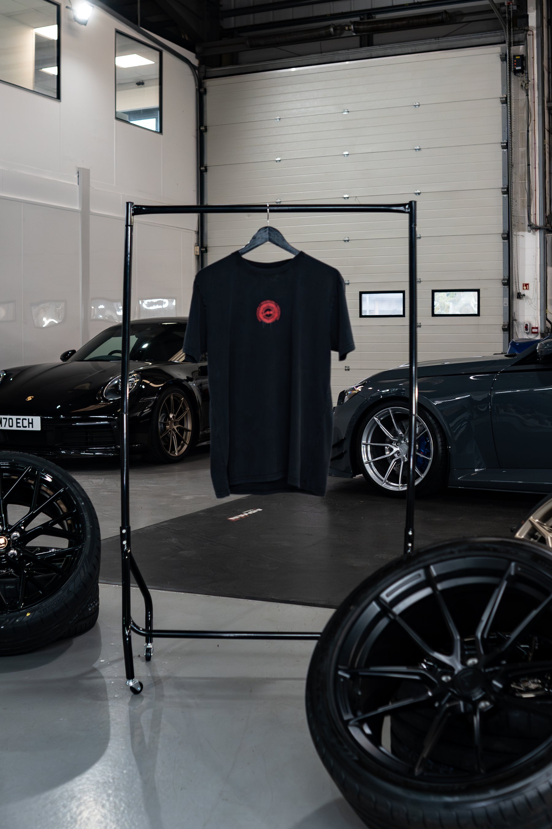 Treadlight Collection Stone Washed T-Shirt with a red logo on a rack in a garage setting with cars and tires.