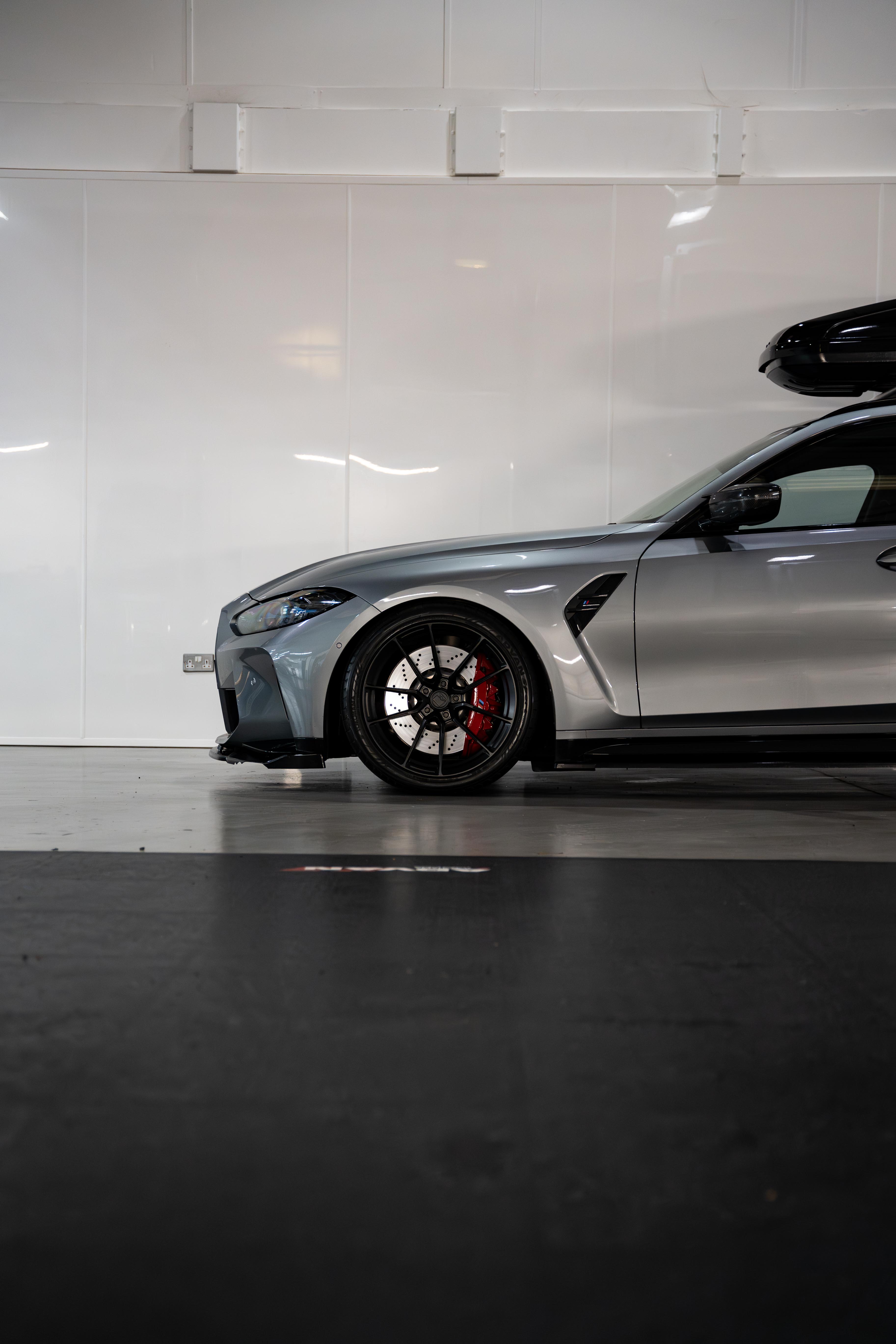 Front of a Grey G81 M3 Touring with a roof box & is sat on Motech stance springs - parked in a workshop.