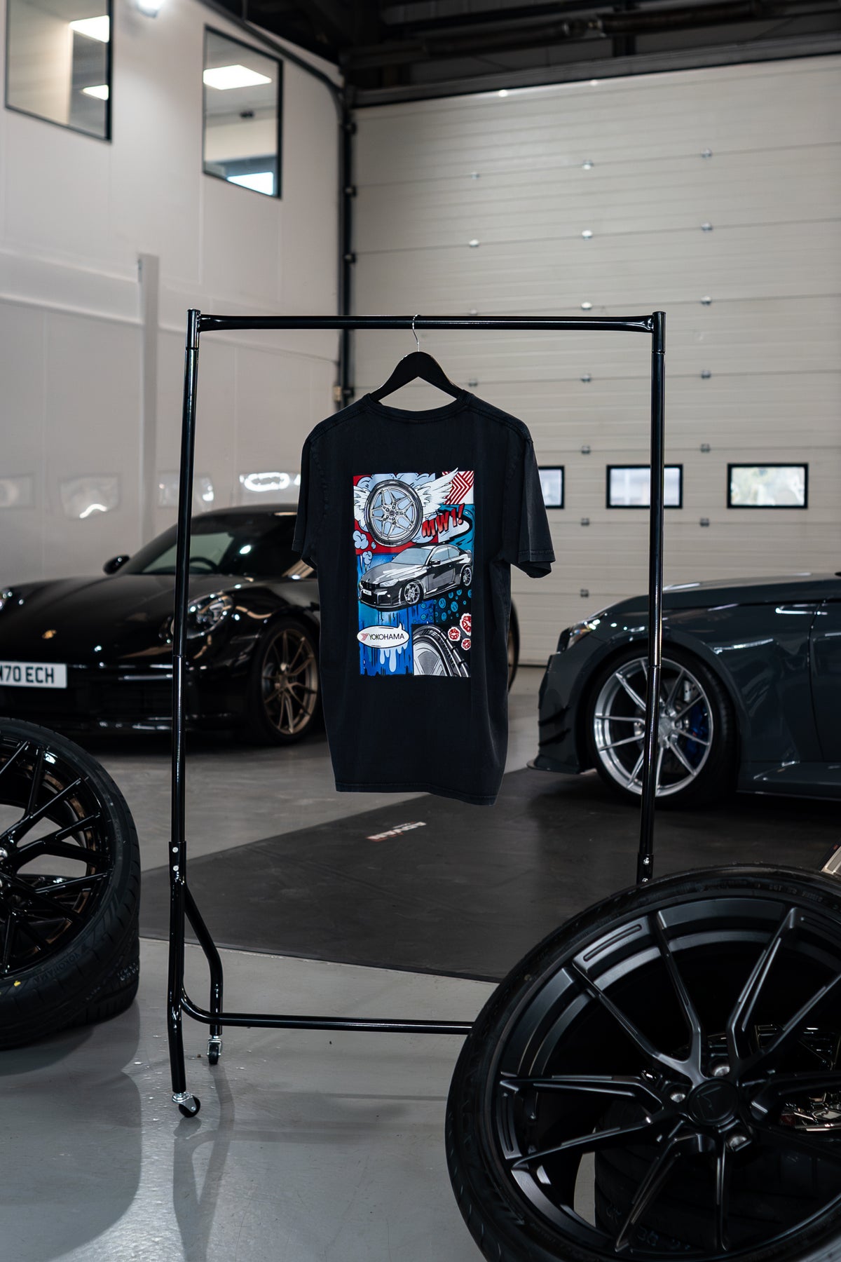 Treadlight Collection Stone Washed T-Shirt with graphic design on a rack in a garage setting with cars and tires.