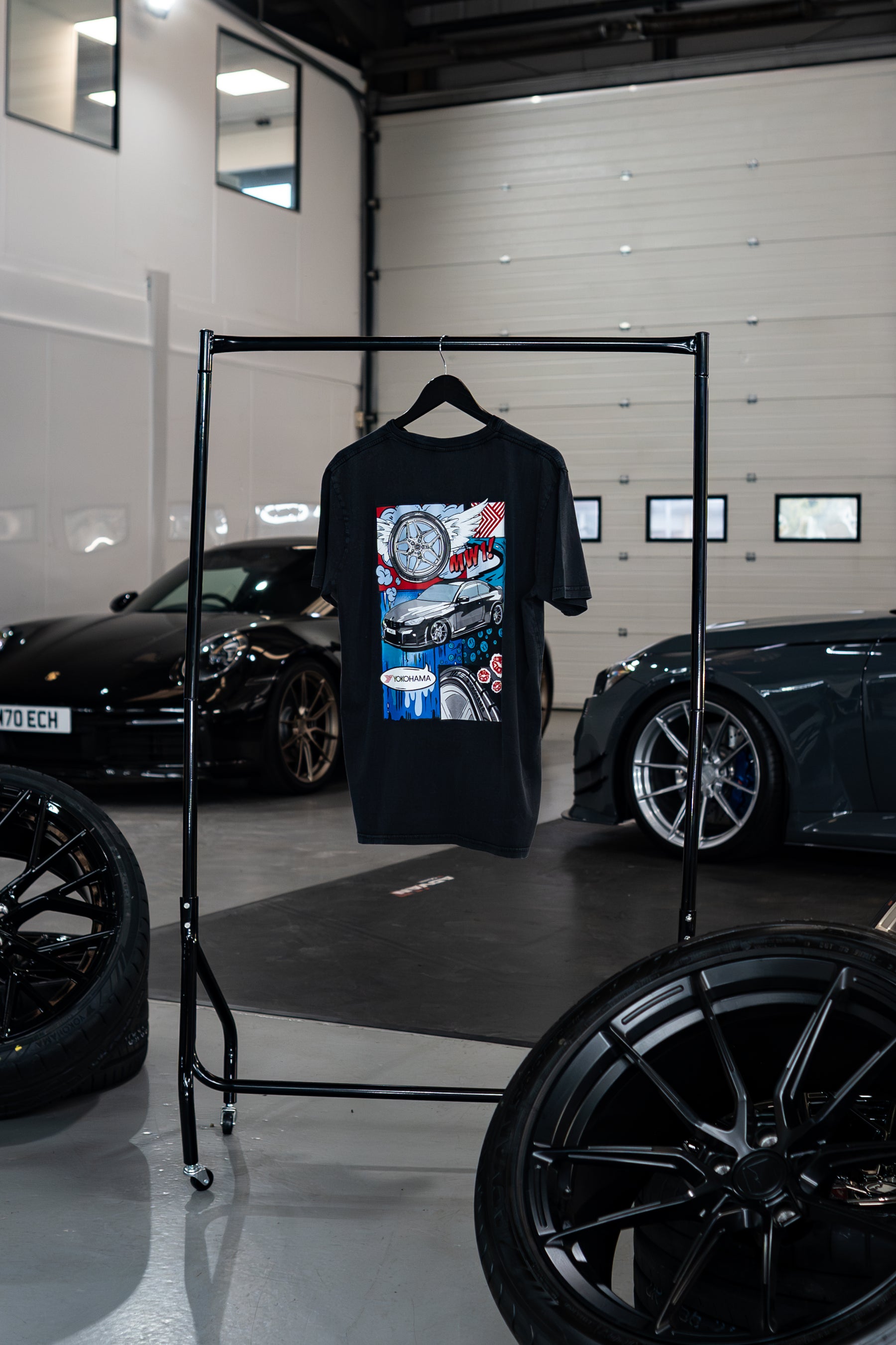 Treadlight Collection Stone Washed T-Shirt with graphic design on a rack in a garage setting with cars and tires.