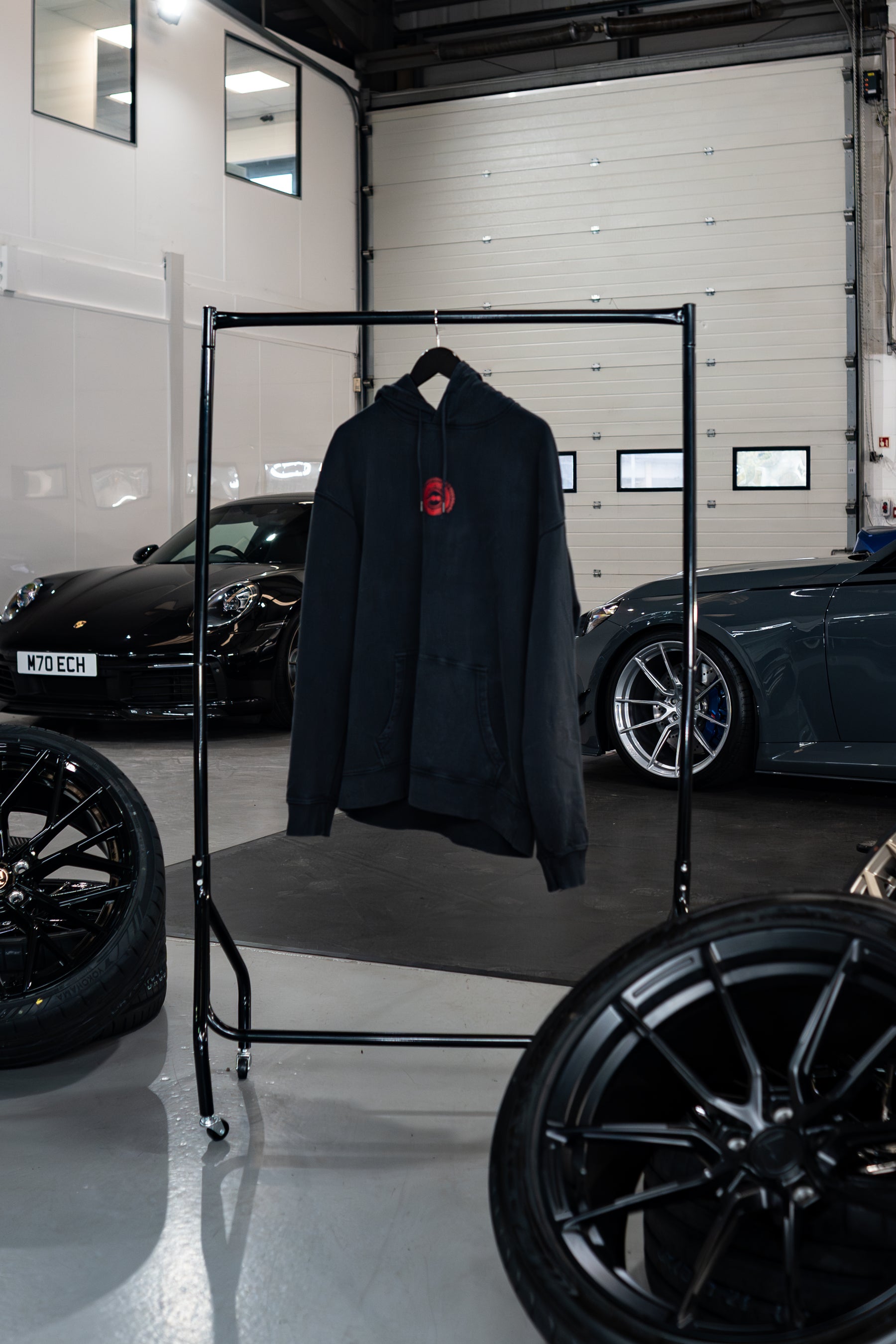 Stone-washed Treadlight collection Motech hoodie with a red logo on a rack in a garage setting with cars and tires.