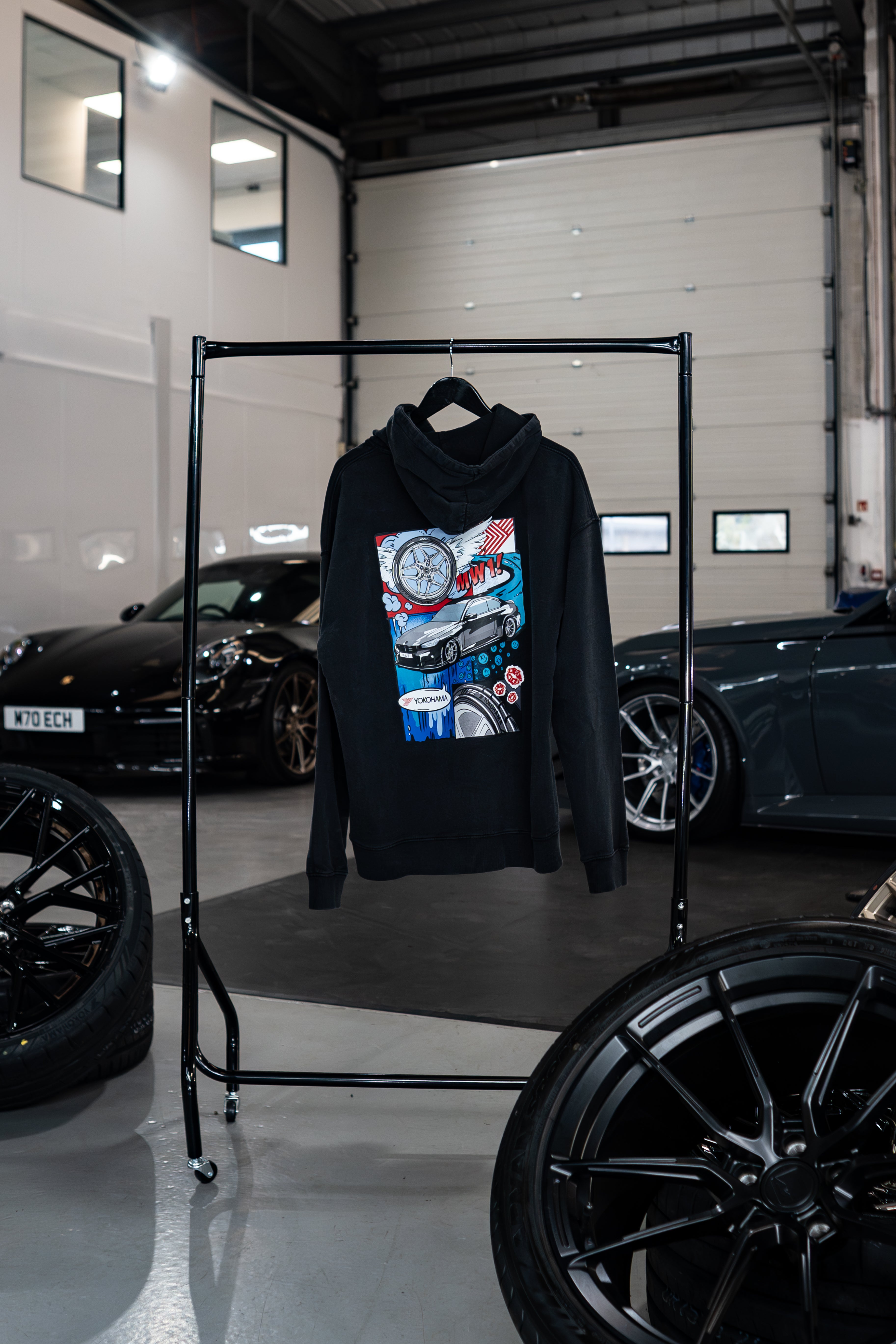 Stone-washed Treadlight collection Motech hoodie with graphic design on a rack in a garage setting with cars in the background