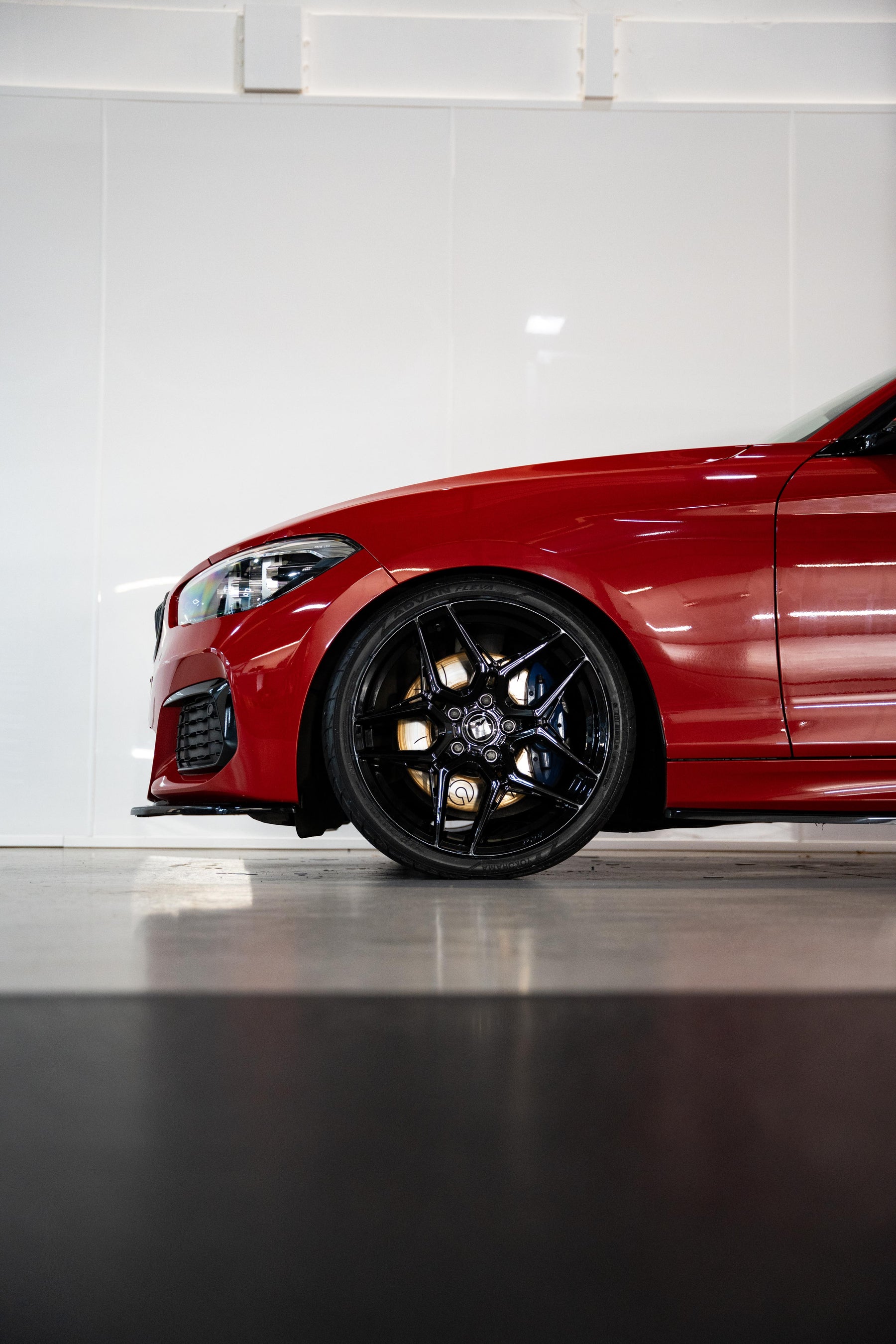 Front of a red BMW with Precision Black M-W1's in a workshop.
