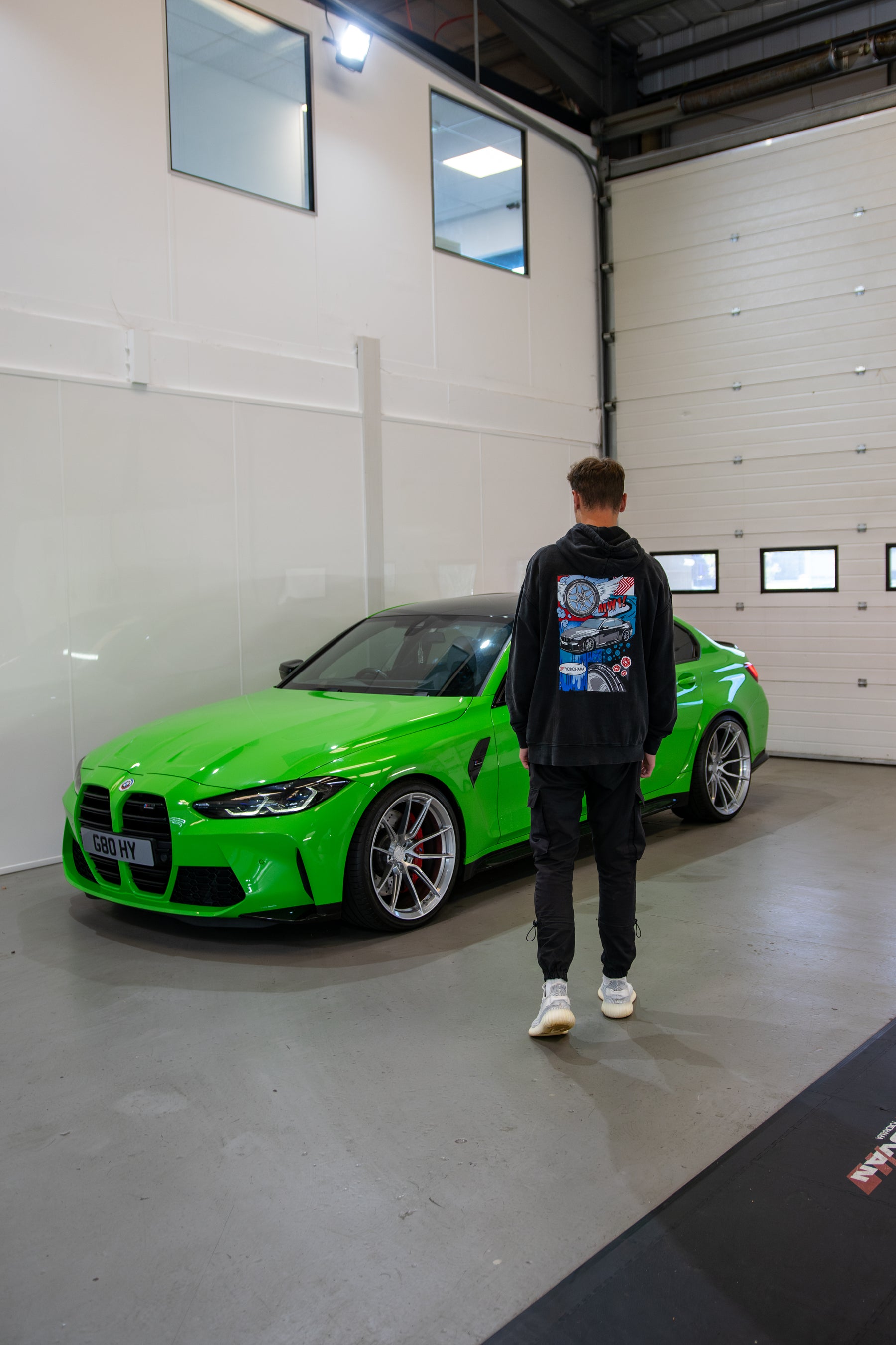 Person wearing a Stone-washed Treadlight collection Motech hoodie next to a bright green car in a garage