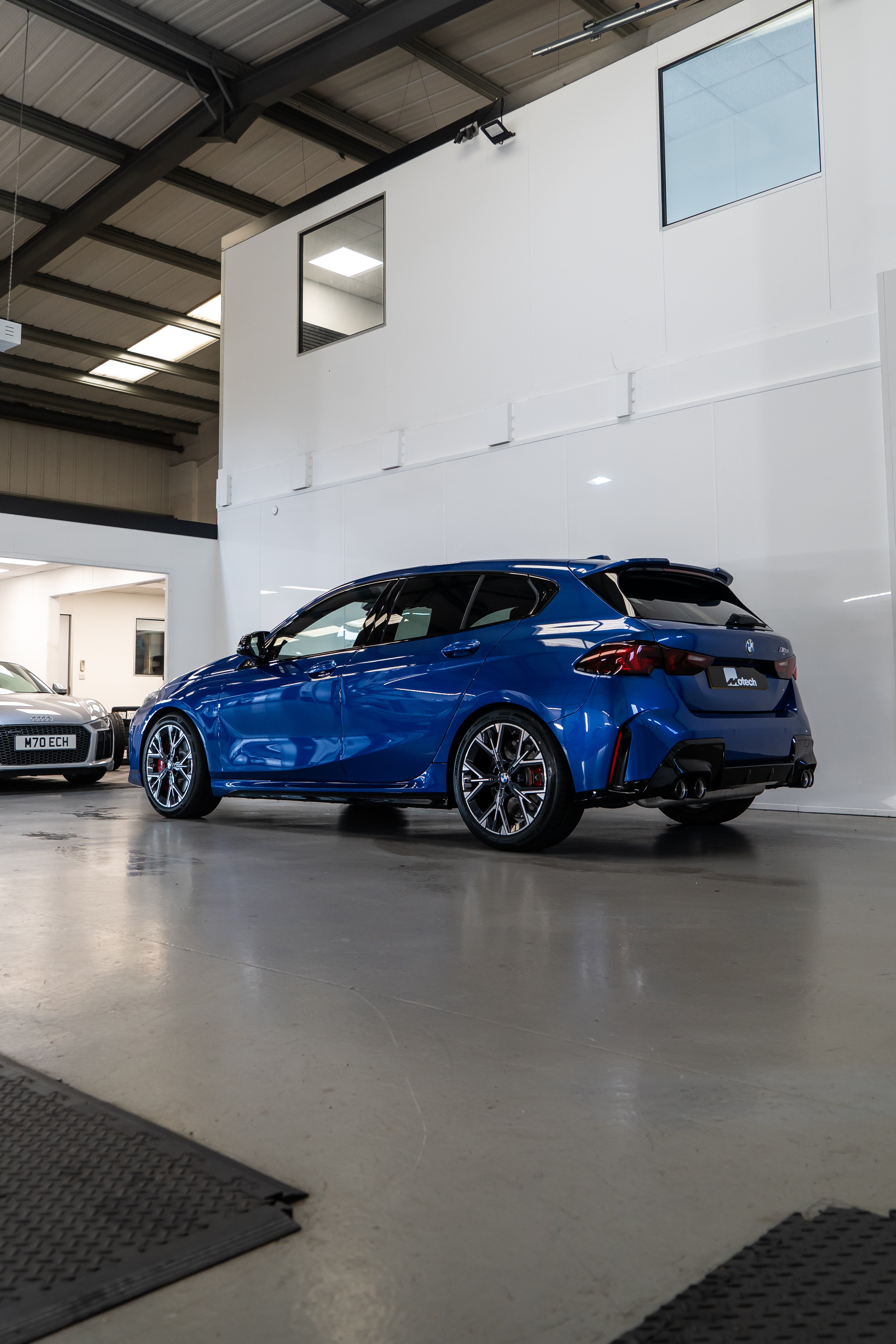 Side-on shot of a BMW F70 with Motech stance springs parked in a car workshop.