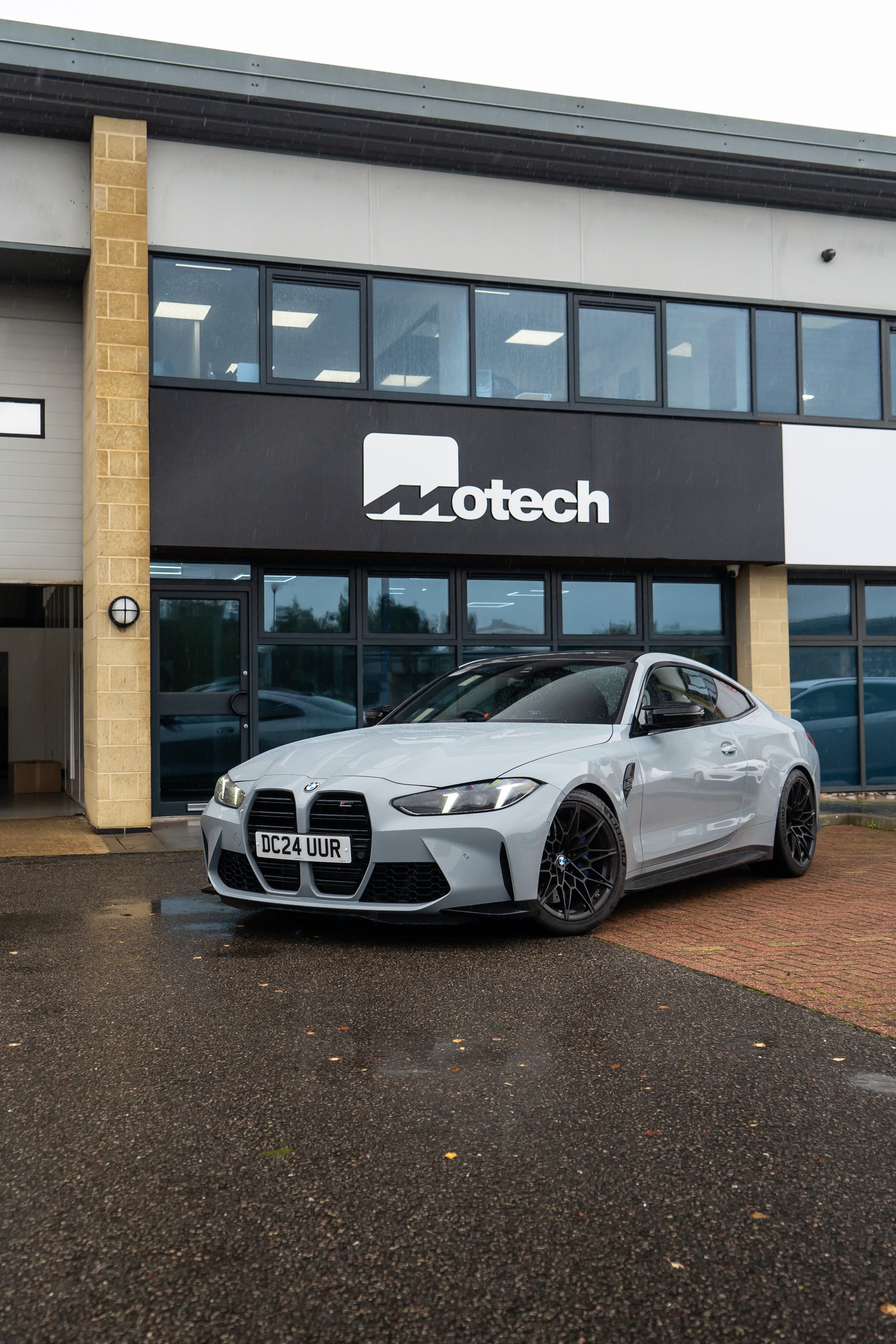 Grey BMW M4 on Motech stance springs parked outside a building with 'Motech' branding.