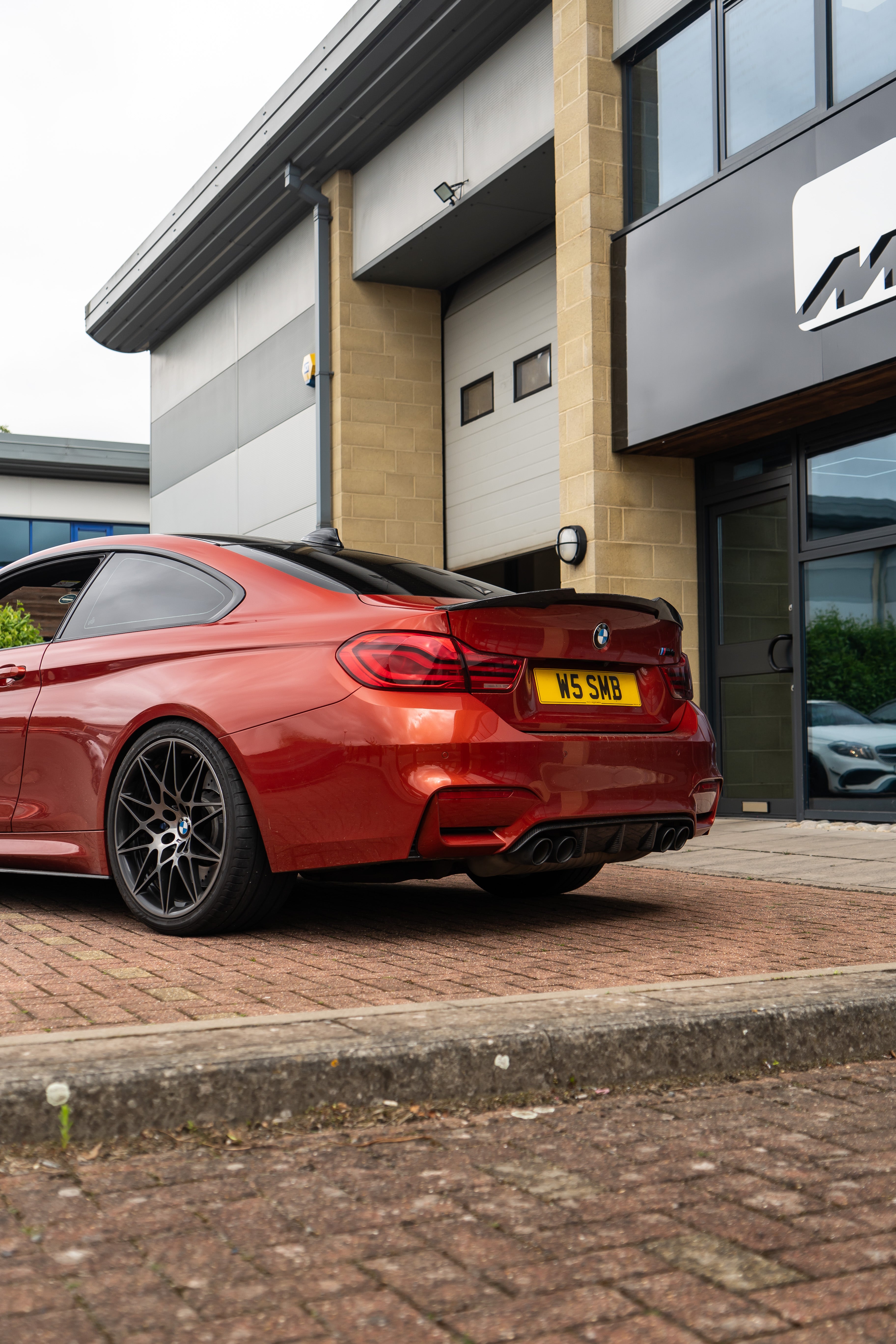 Back of a Red BMW M4 on Motech stance springs parked outside 'M' branded building