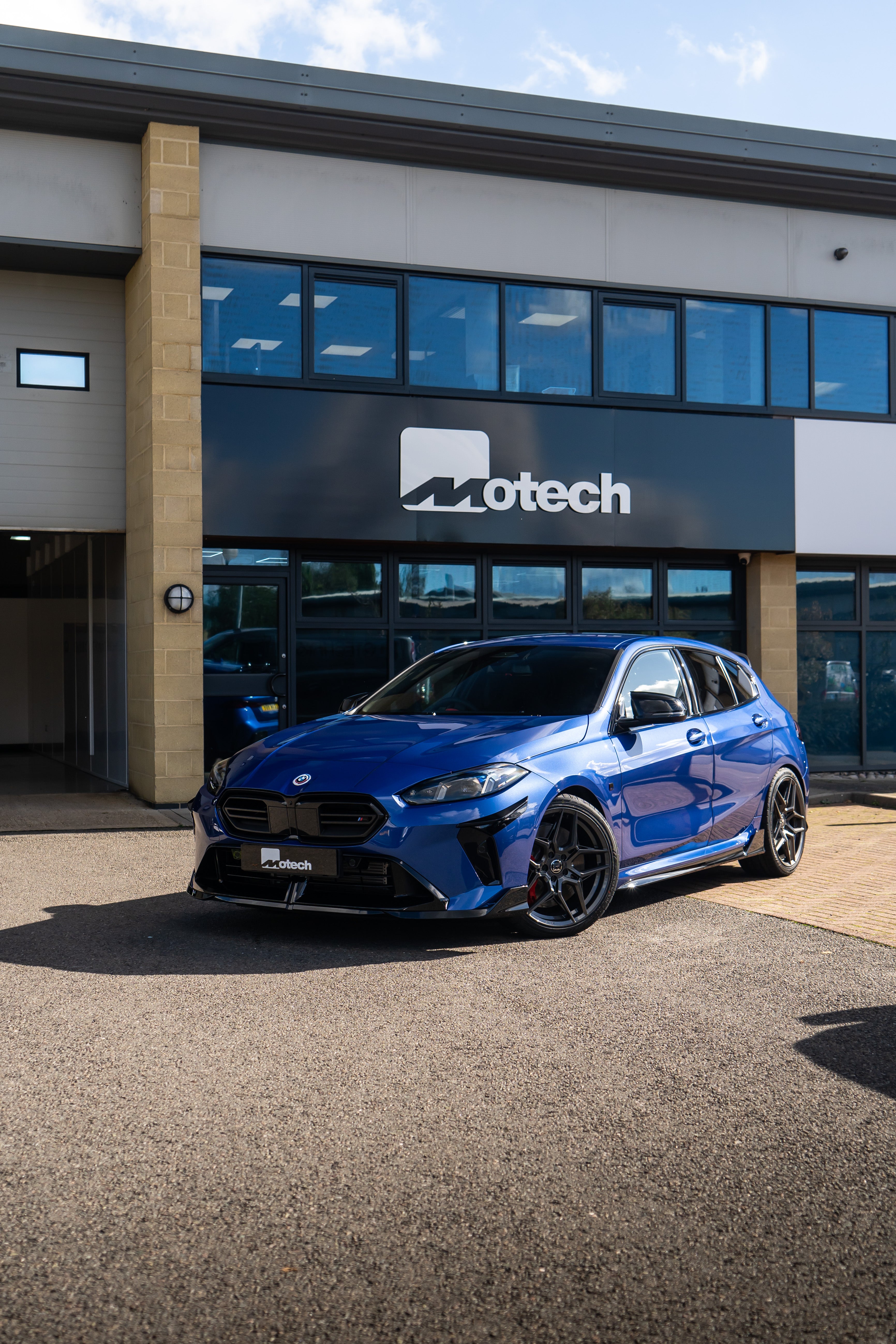 Blue BMW F70 with Motech wheels on Motech stance springs parked outside a building with 'Motech' branding.