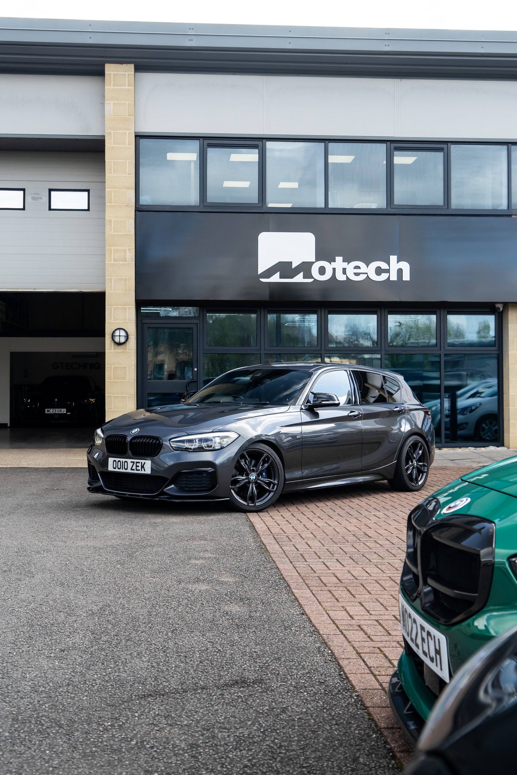 Grey BMW 1 Series on Motech Stance Springs parked outside a building with 'Motech' branding.