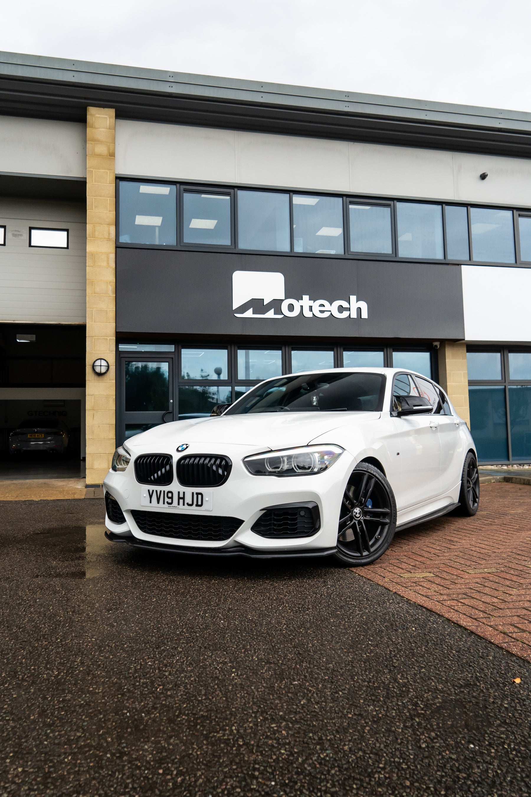 White BMW 1 Series on Motech stance springs parked outside a building with 'Motech' branding.