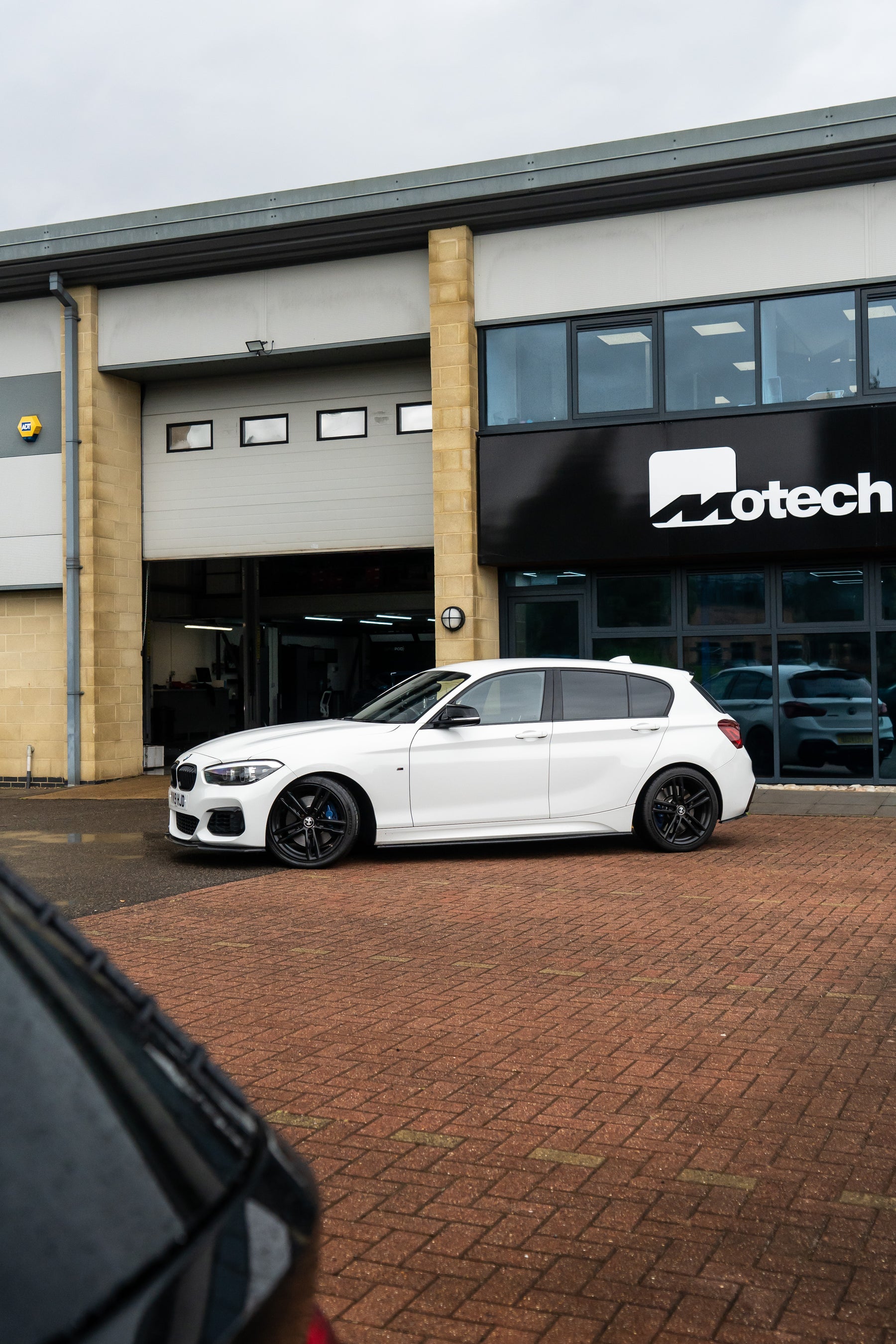 A white BMW 1 Series with Motech stance springs outside the Motech building.