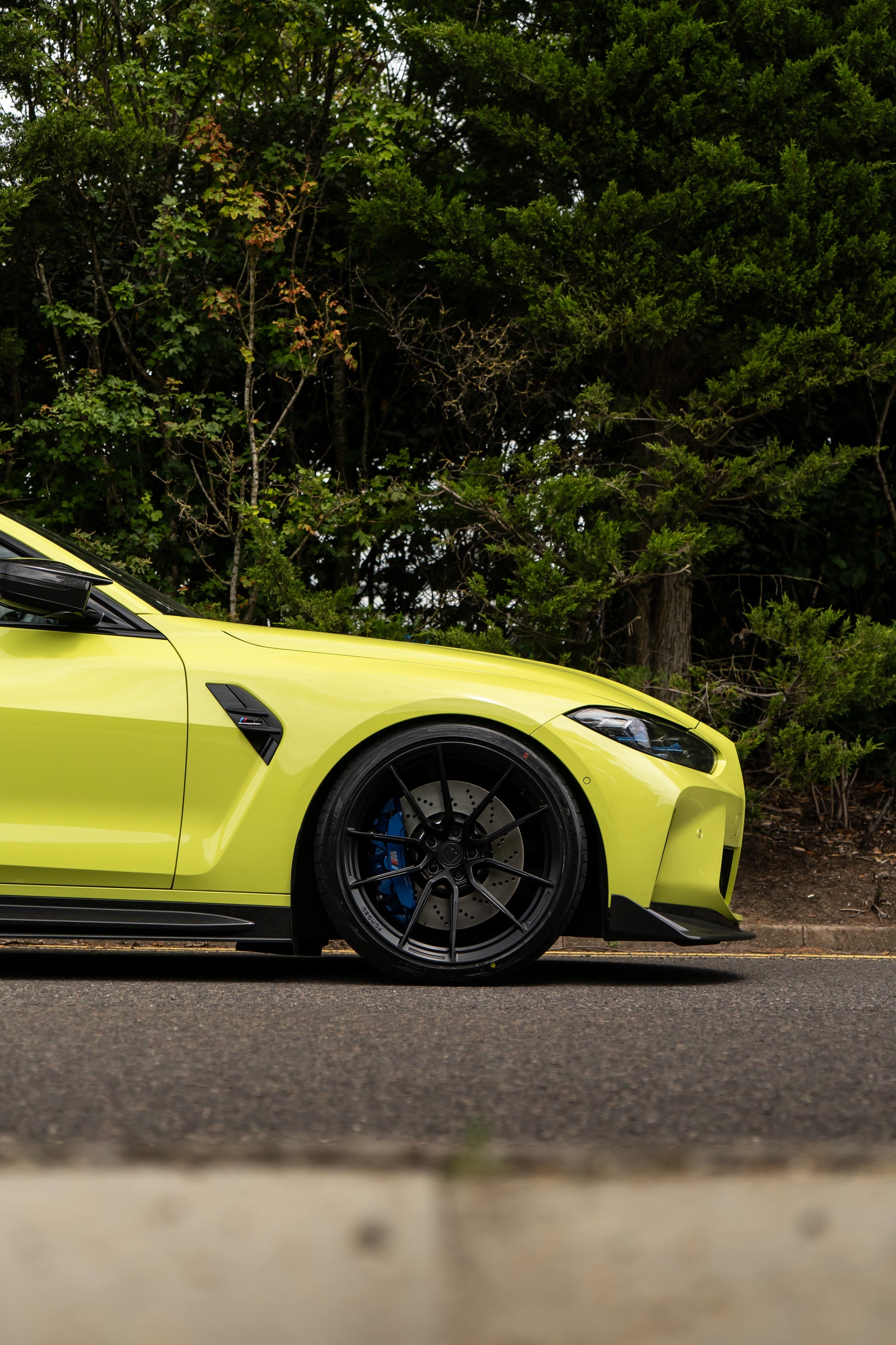 Front of a São Paulo Yellow BMW M4 on Motech Stance Springs parked in front of some trees.
