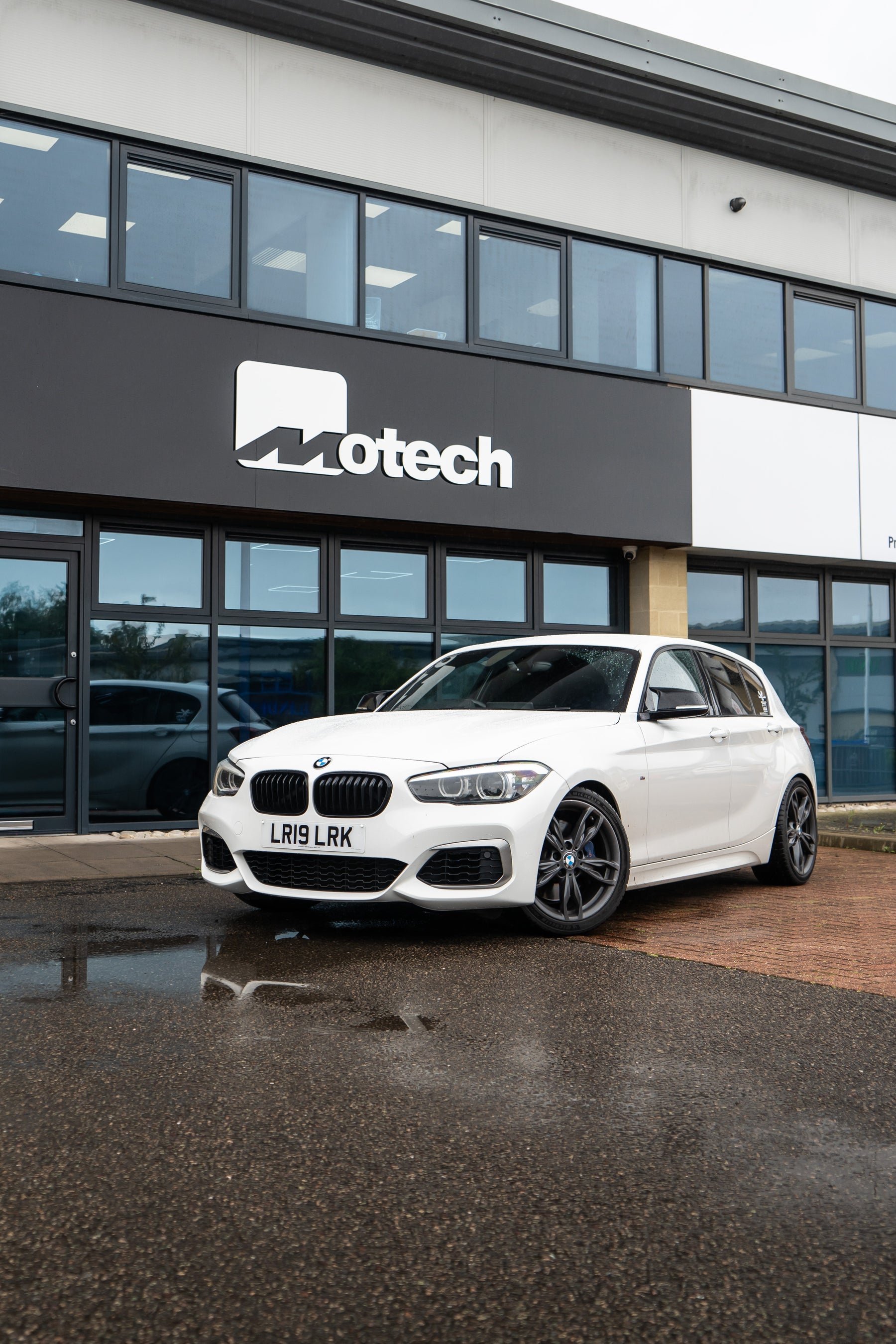 White BMW on Motech Stance Springs parked outside a building with 'Motech' branding.