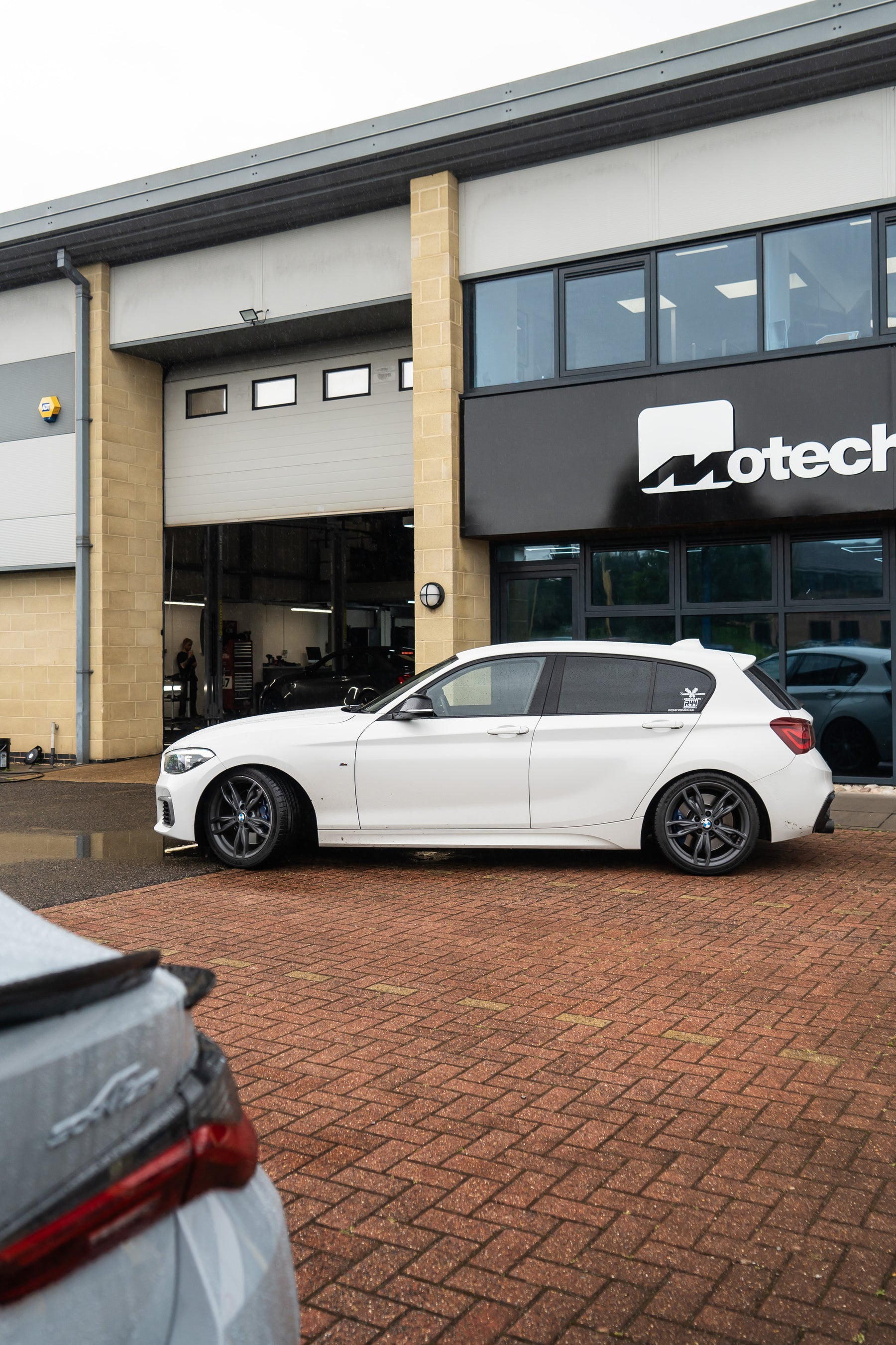 Side-on shot of a white BMW with Motech Stance Springs parked outside a building with 'Motech' branding.