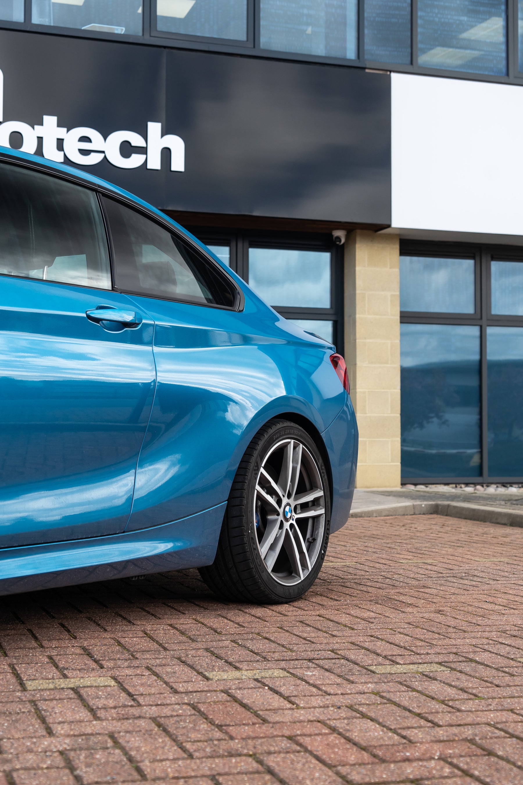 Back of a blue BMW on Motech Stance Springs outside a building with 'Motech' branding.