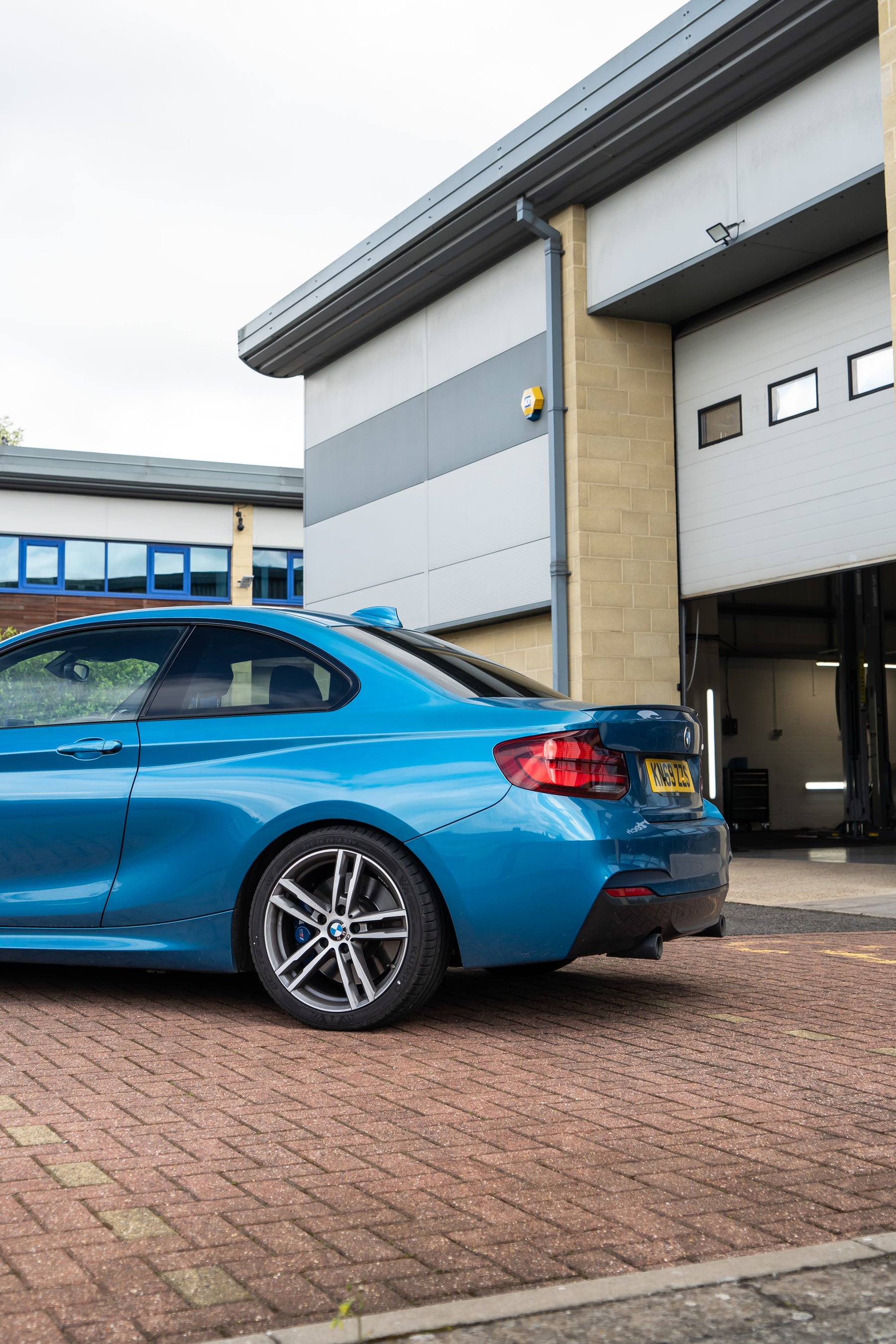 Back of a blue BMW on Motech Stance Springs outside a car garage.