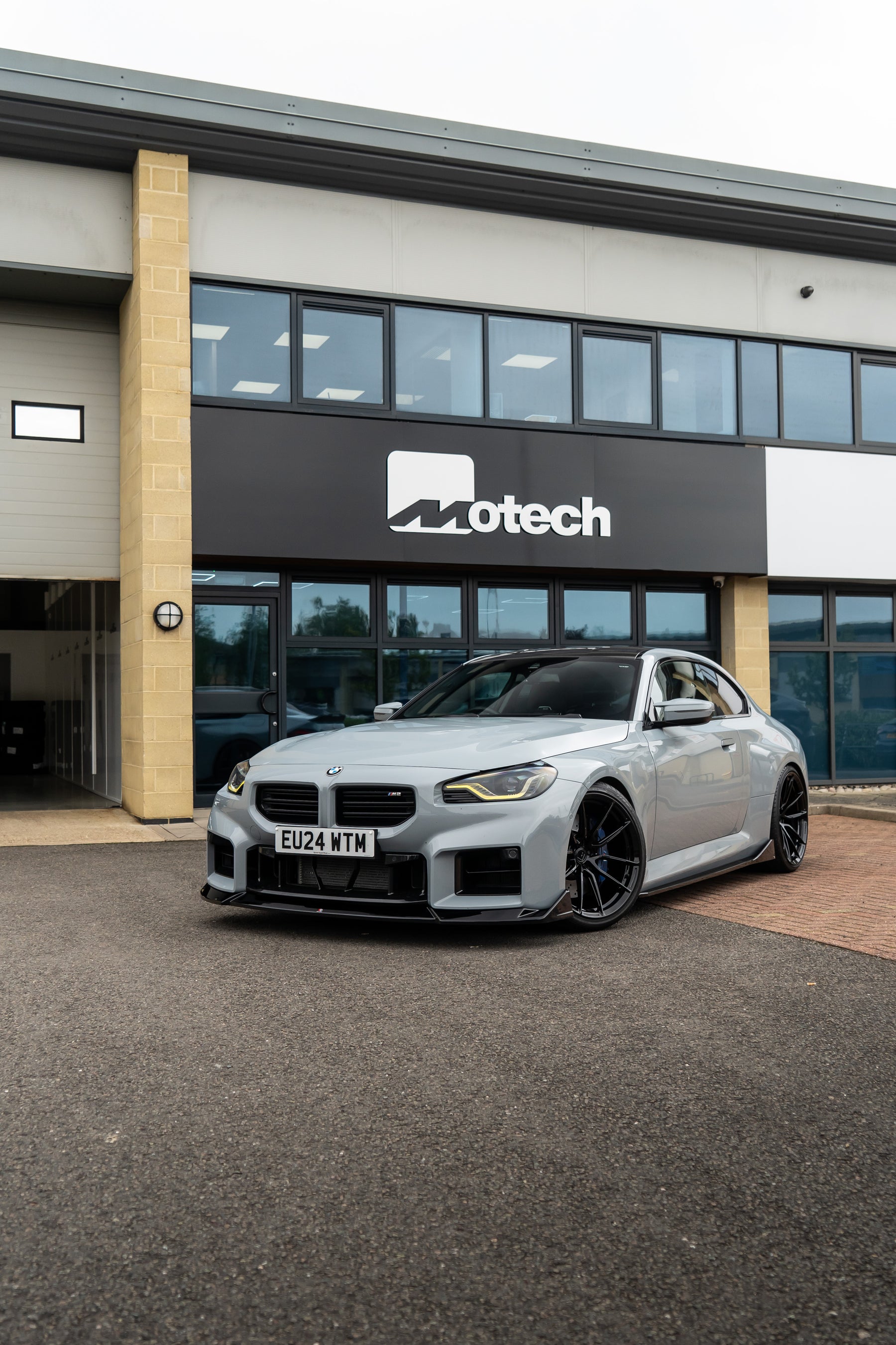 Grey BMW M2 G87 on Motech Stance Springs parked outside a building with 'Motech' branding.