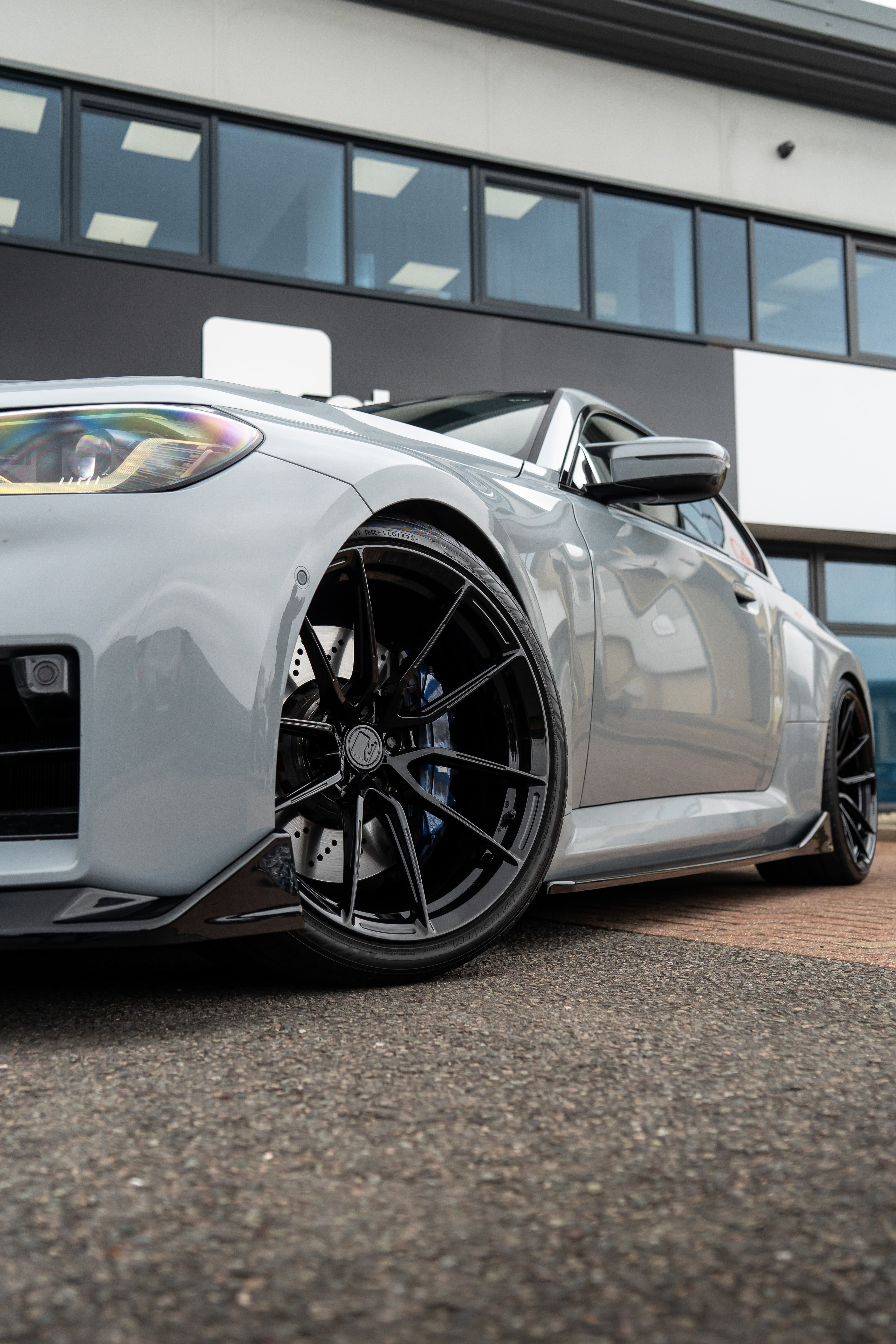 Close-up shot of a black M-W4 on a Grey BMW M2 G87 on Motech Stance Springs parked outside a building.