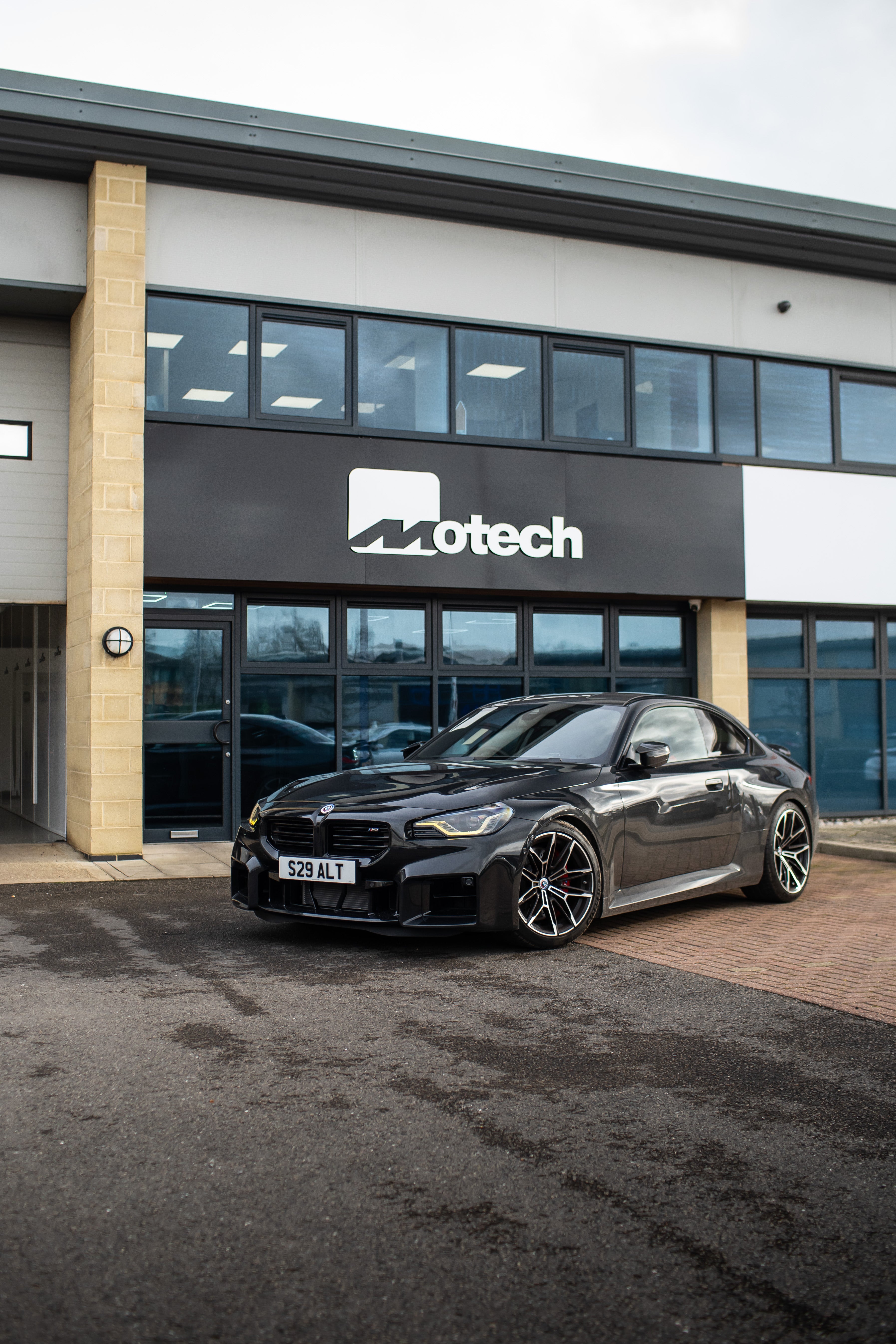 Black BMW M2 G87 on Motech Stance Springs parked outside a building with 'Motech' branding.