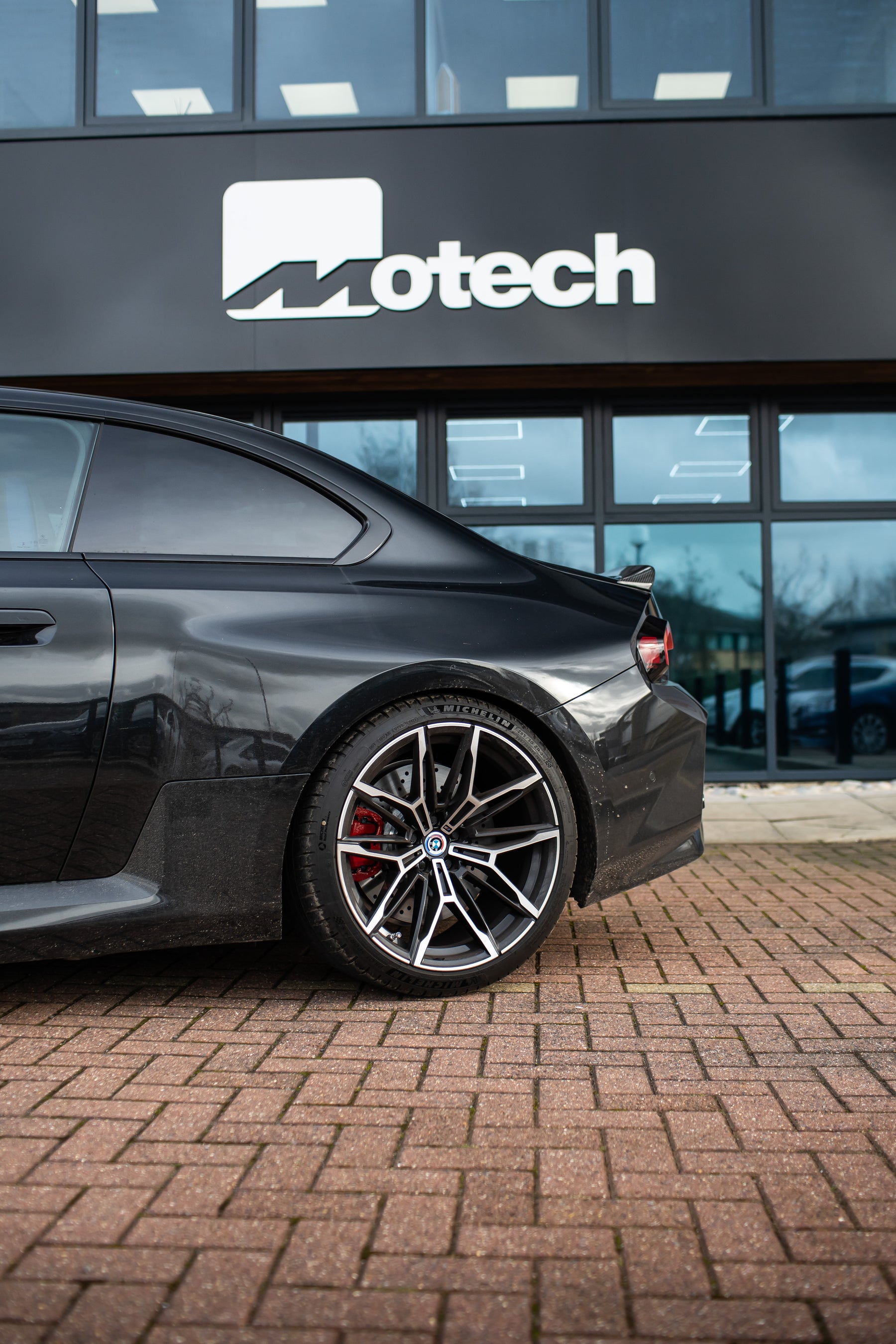 The back of a Black BMW M2 G87 on Motech Stance Springs parked outside a building with 'Motech' branding.