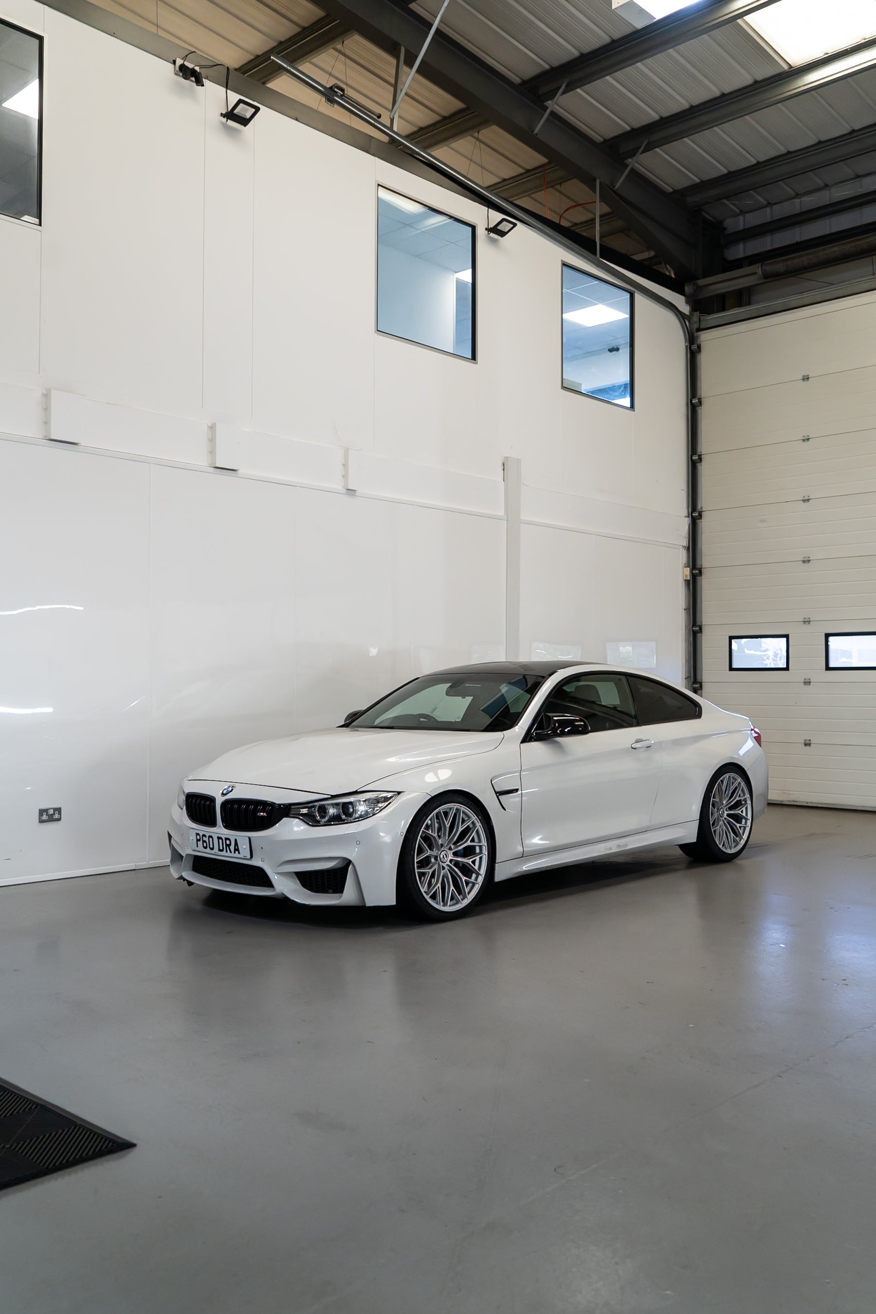 White BMW car inside a large industrial garage with white walls and a concrete floor.