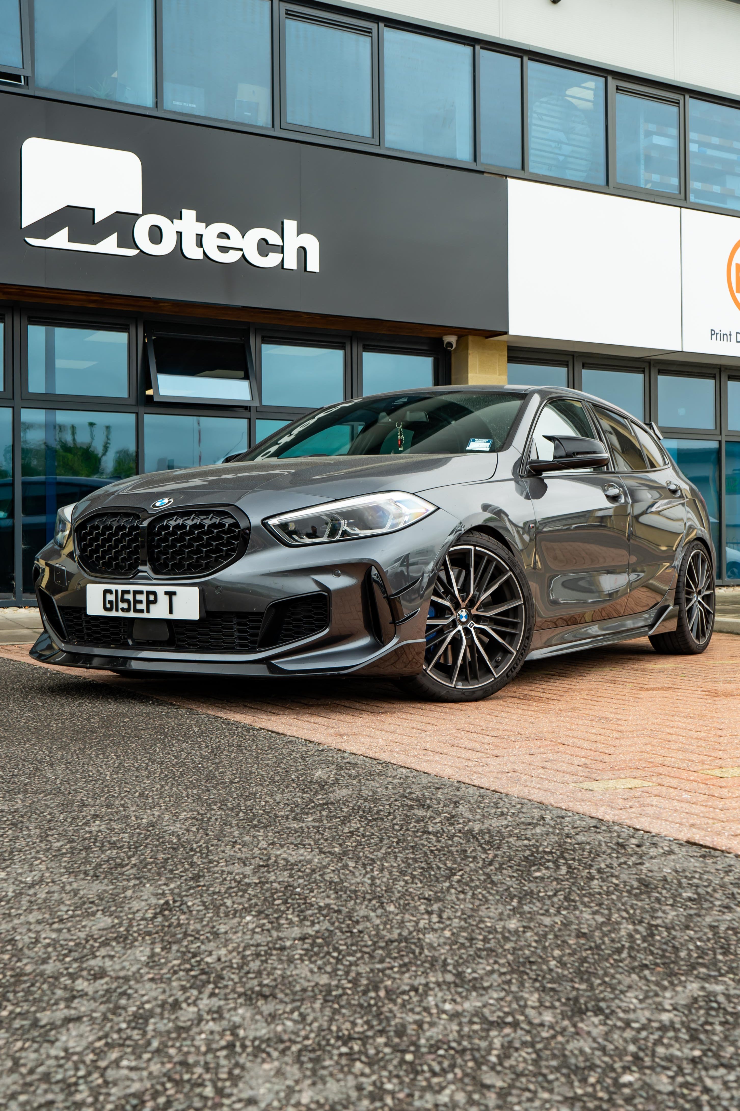 Grey car parked in front of a building with 'motech' branding.