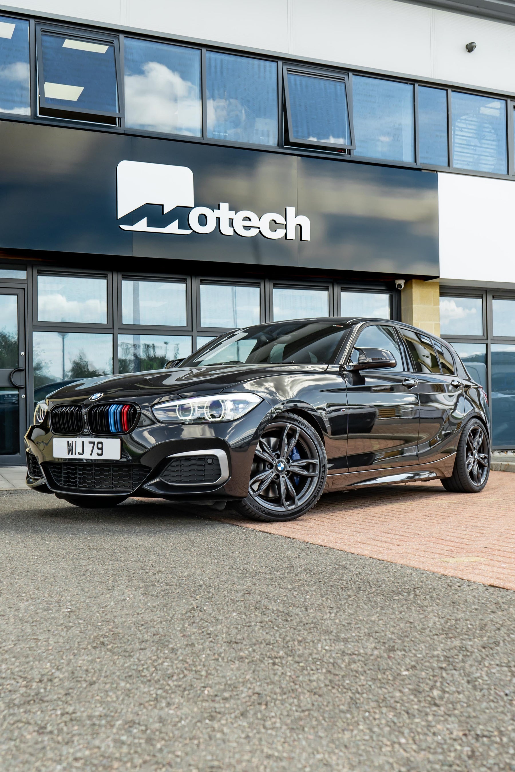 Black BMW 1 Series on Motech Stance Springs parked outside a building with 'Motech' branding.
