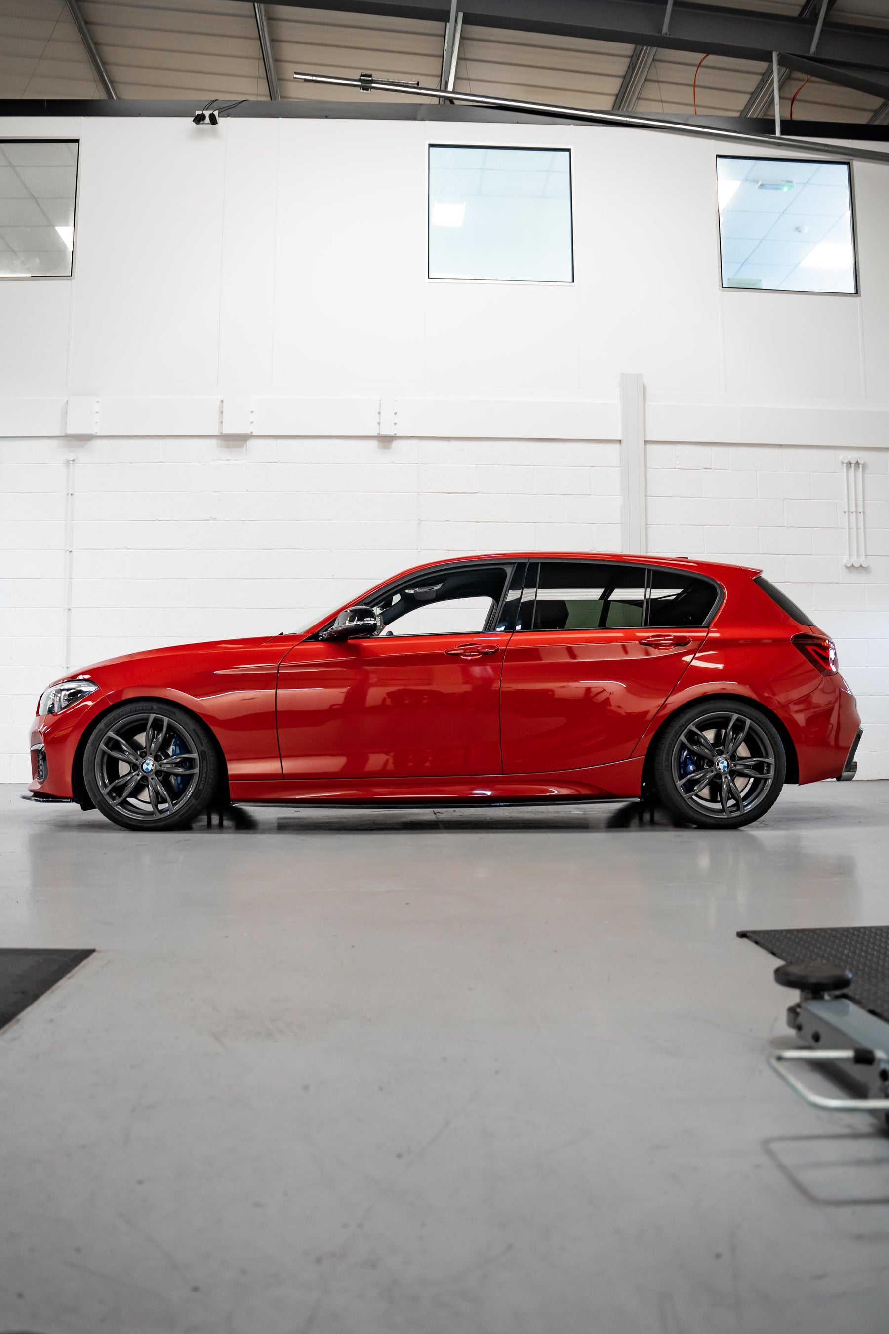 A side-on shot of a red BMW 1 Series on Motech Stance Springs parked inside a workshop.
