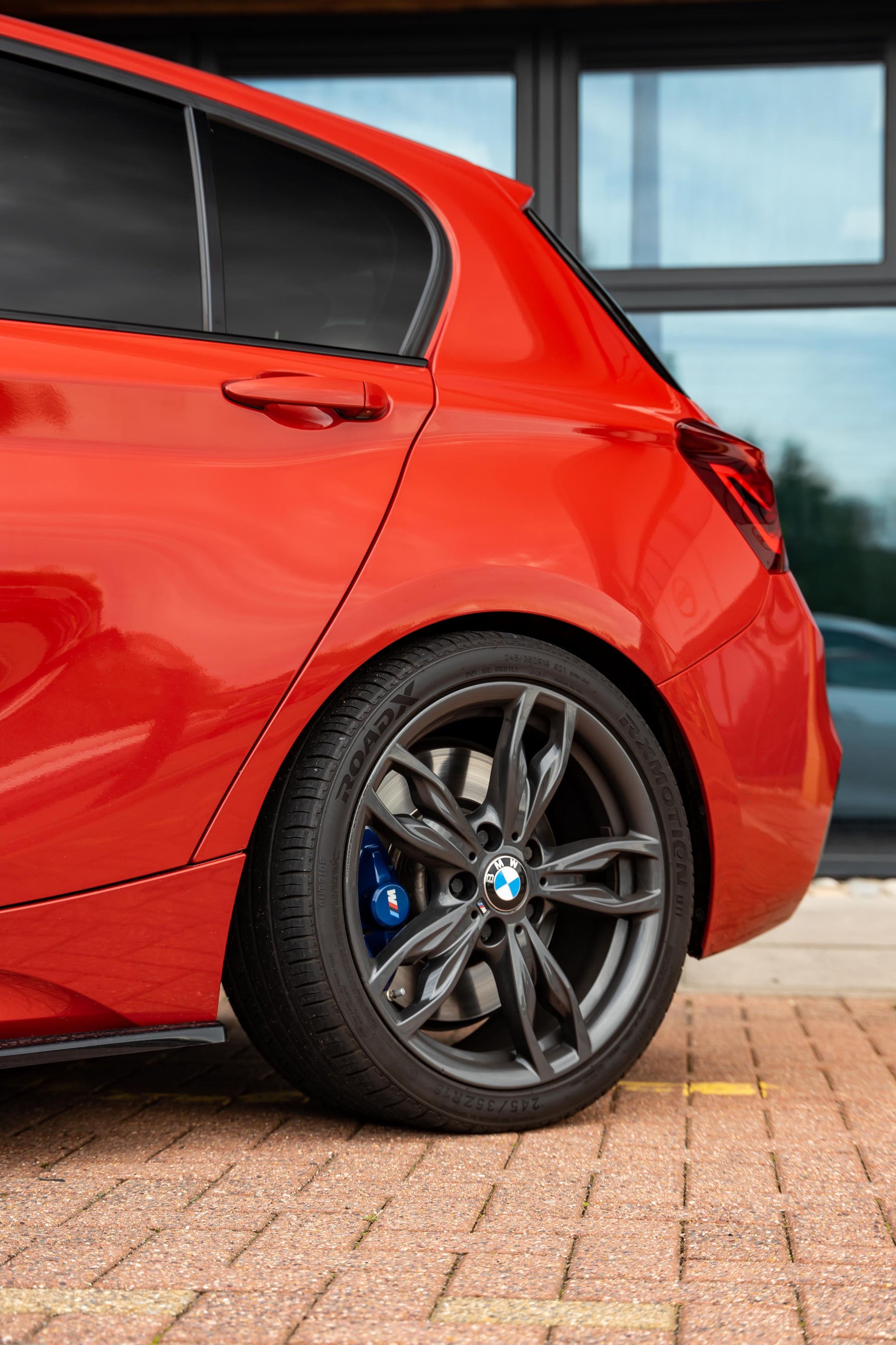 The back of a red BMW 1 Series on Motech Stance Springs parked on a red-brick drive.