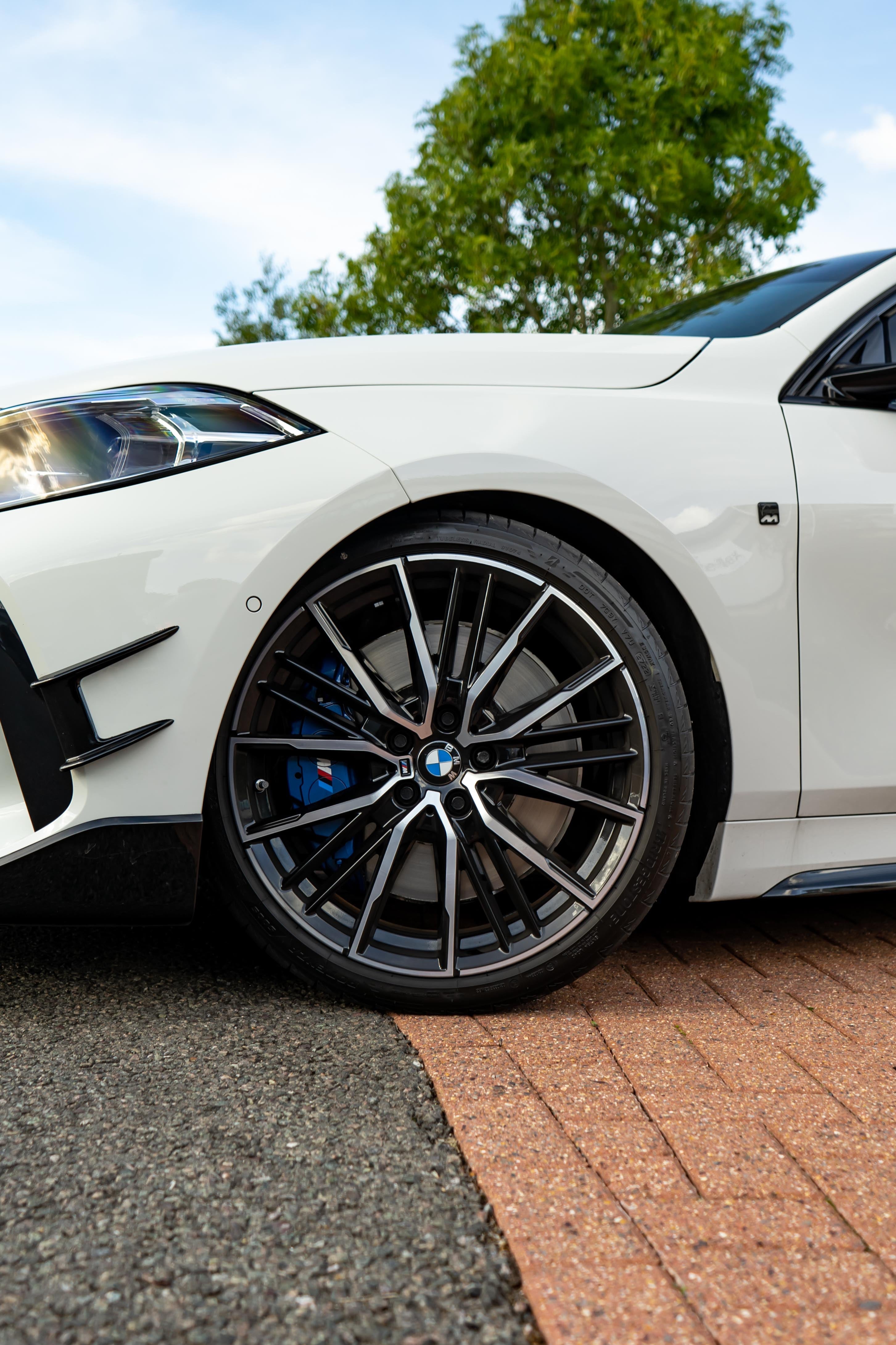 Close-up of a white BMW's wheel with trees in the background