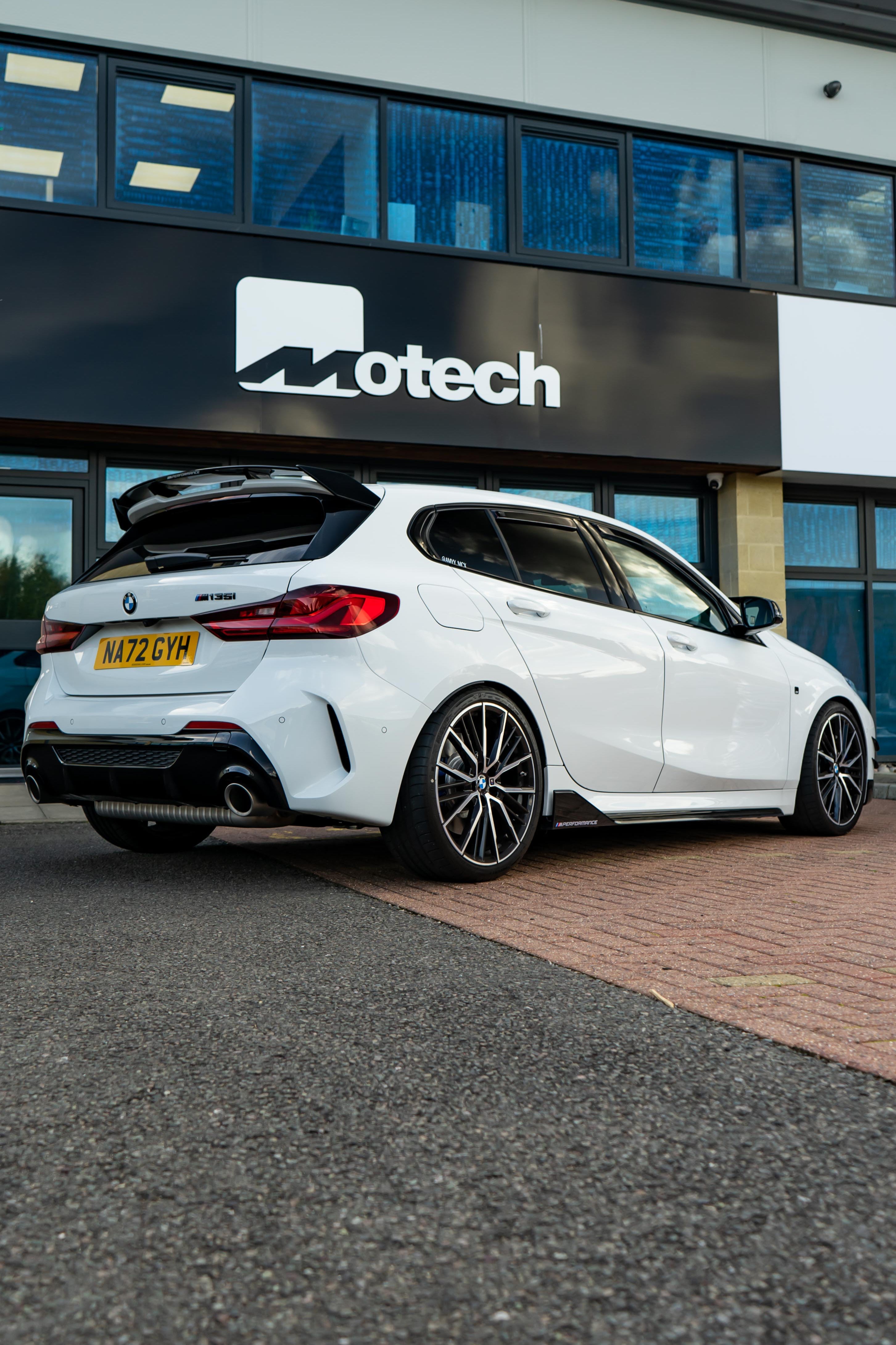 White BMW car parked in front of a building with Motech branding.