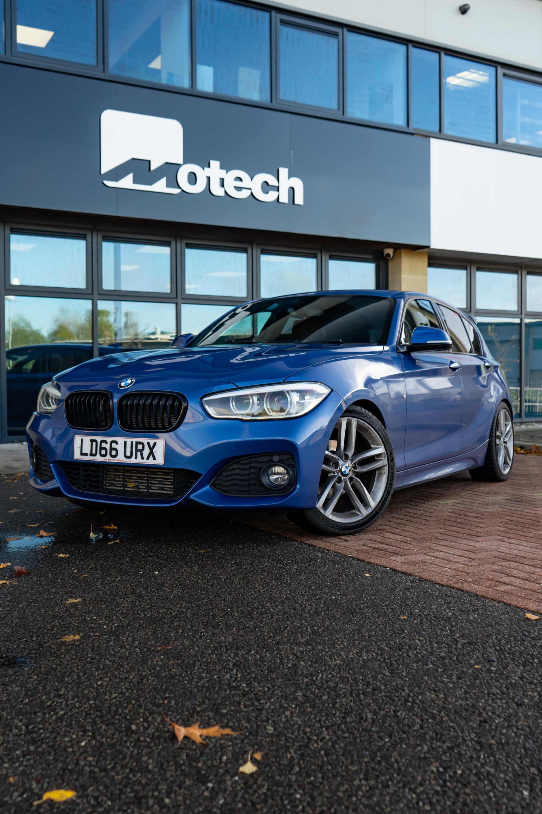 Blue BMW on Motech Stance Springs parked outside a building with 'Motech' branding.