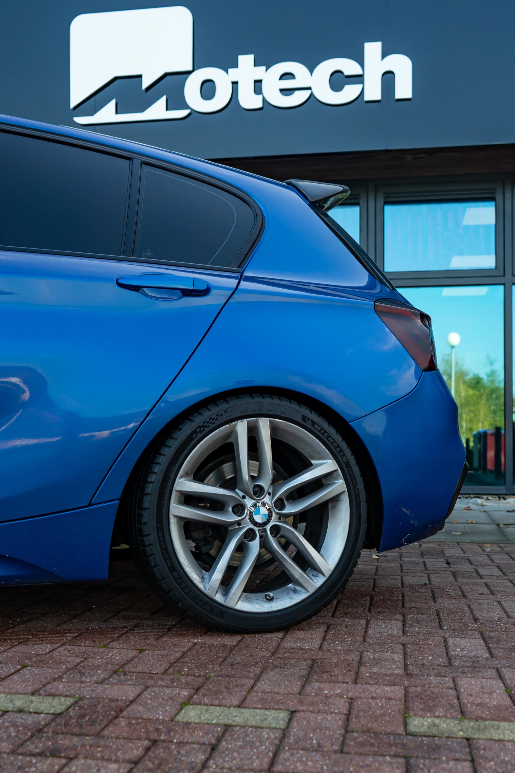 Back of a Blue BMW on Motech Stance Springs parked outside a building with 'Motech' branding.
